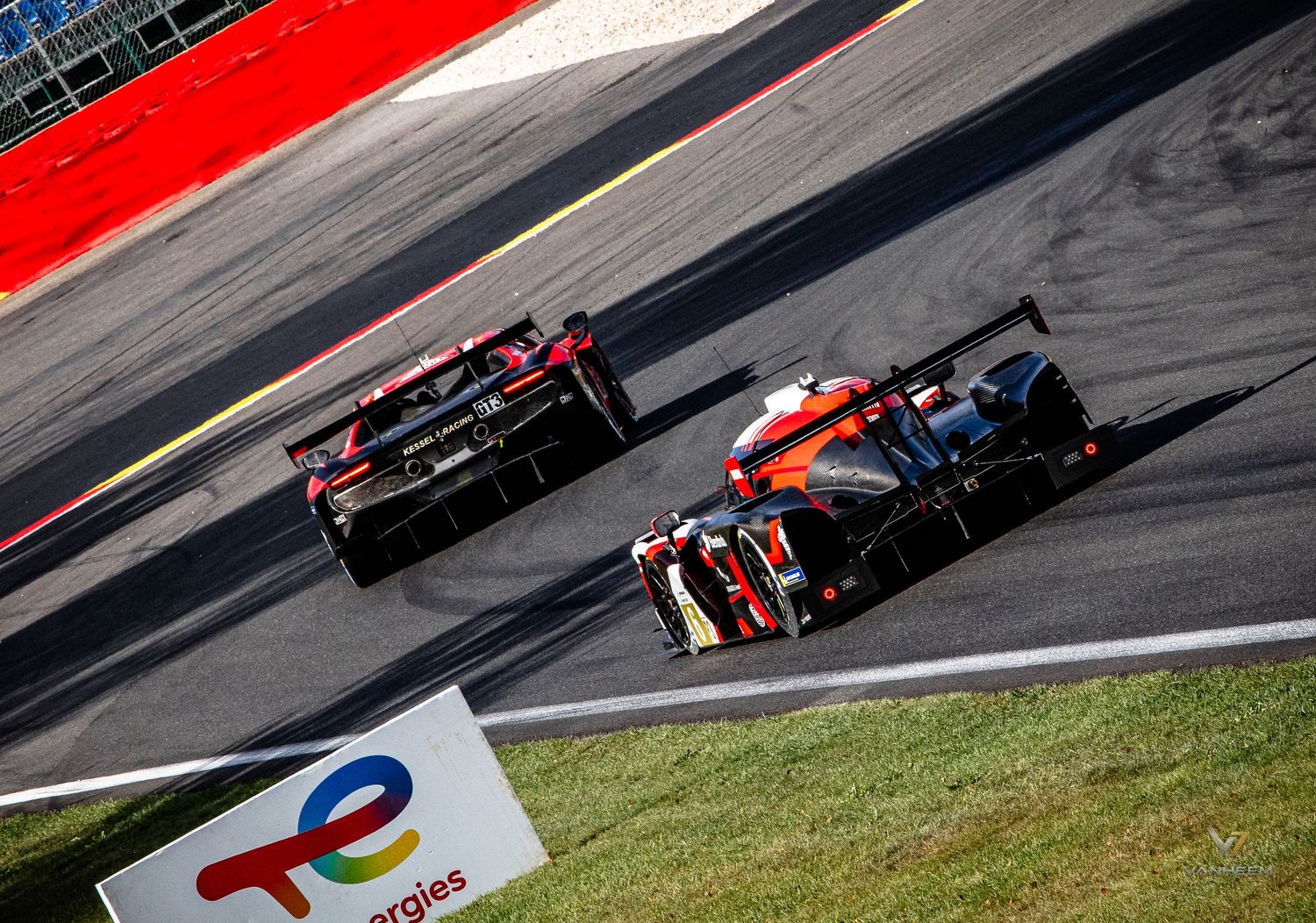 Two LMP racing cars battle on track at a TotalEnergies sponsored circuit during a endurance race.