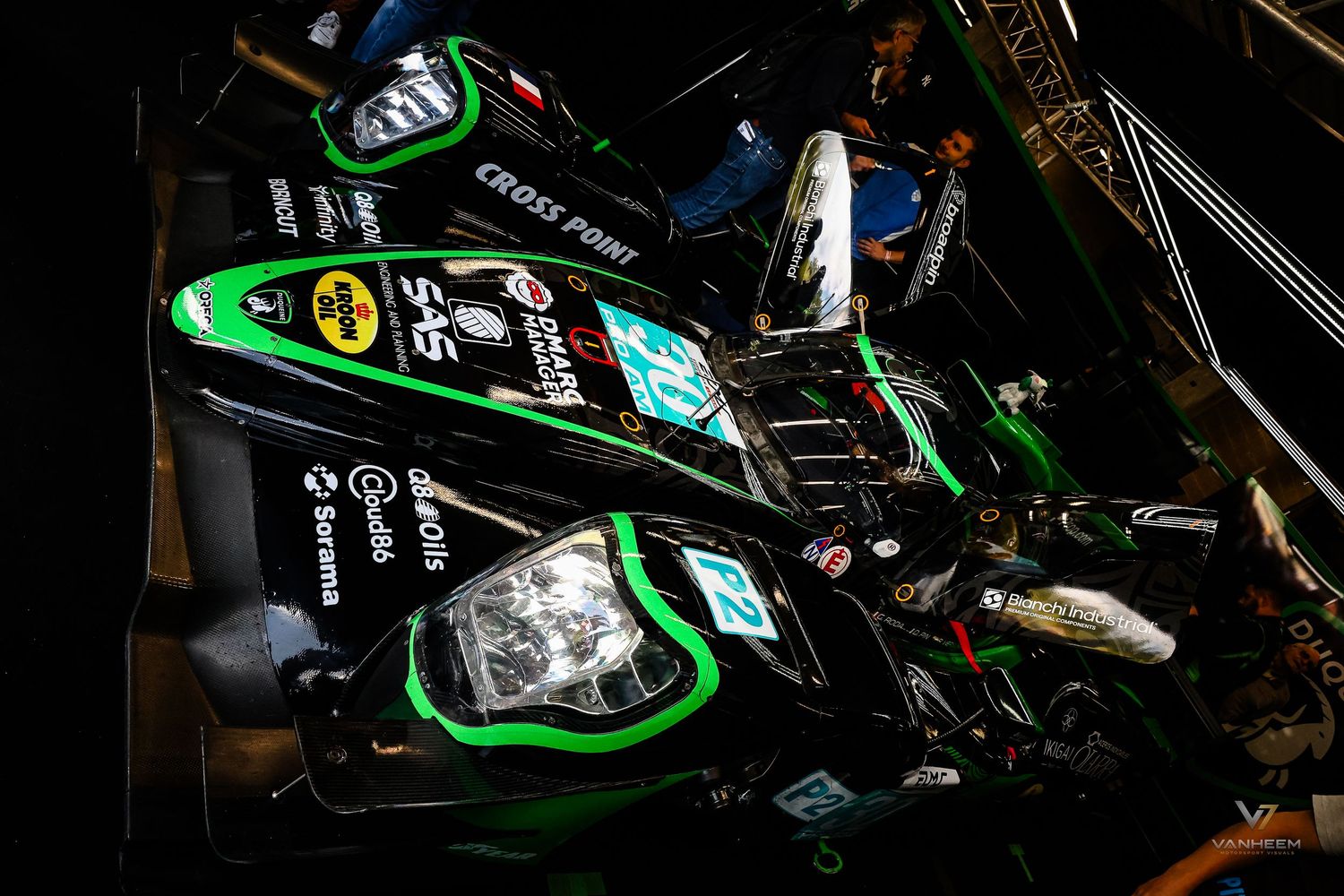 Green and black racing car with Cross Point and SPS sponsorship logos parked in a dimly lit pit lane.