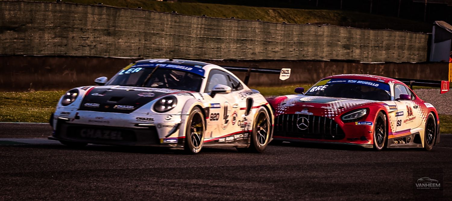 Racing cars speed around a track at dusk with motion blur creating dramatic light trails in the twilight.