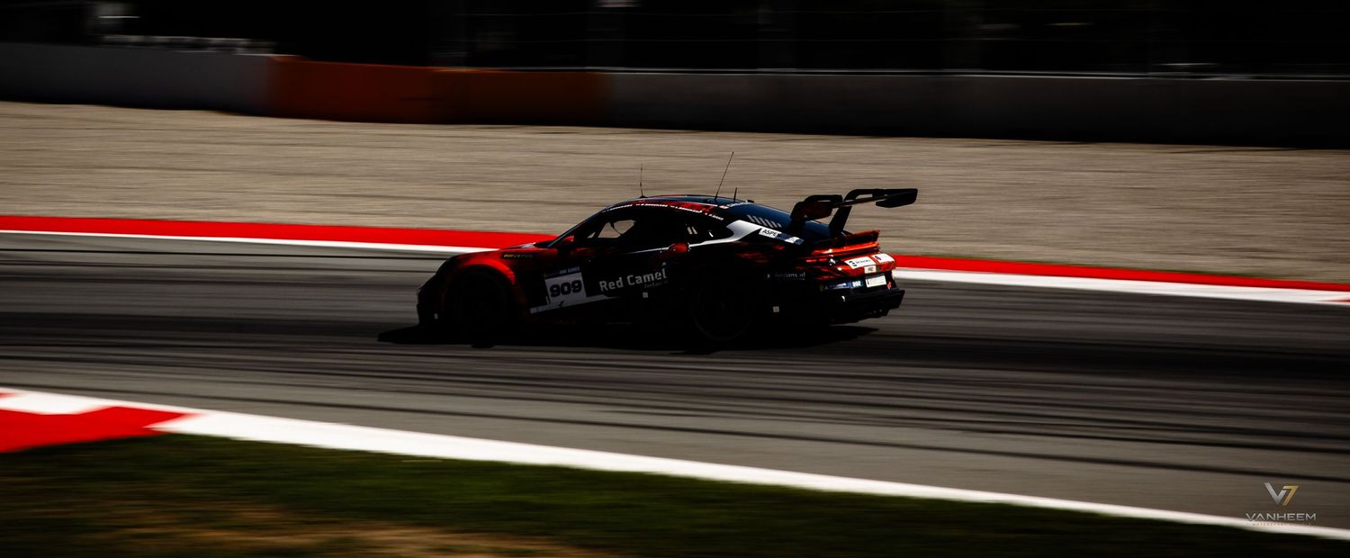 A sleek black and red racing car speeds along a circuit track during a motorsport race event.