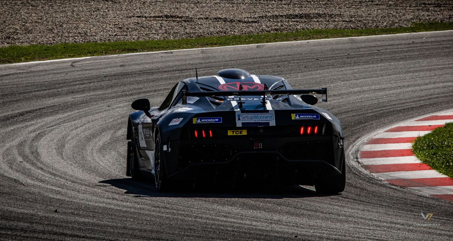 Black GT racing car navigating a curve on a professional motorsport circuit track during a competitive race event.