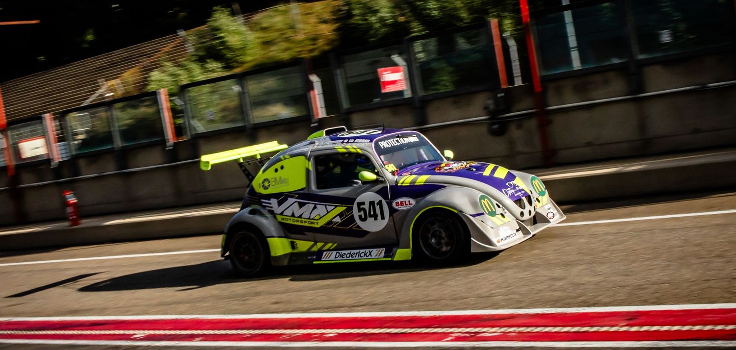Race car number 54 with yellow and white livery speeding on a circuit track during a motorsport event.