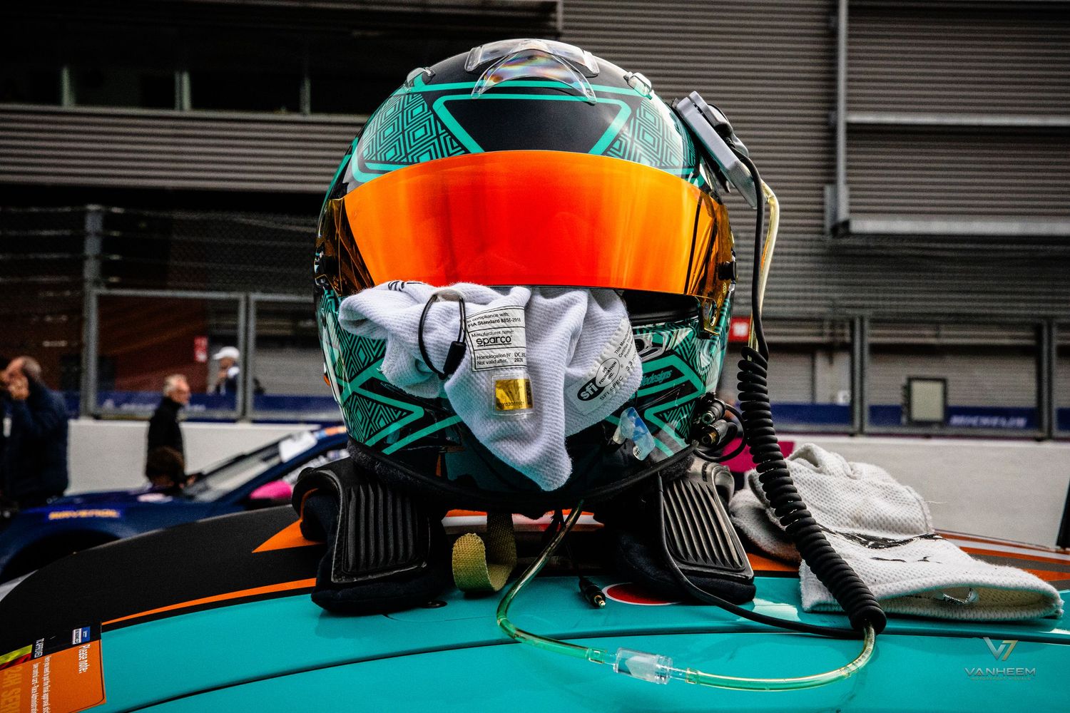 Close-up of a teal and orange racing helmet resting on a Formula E car in the pit garage.