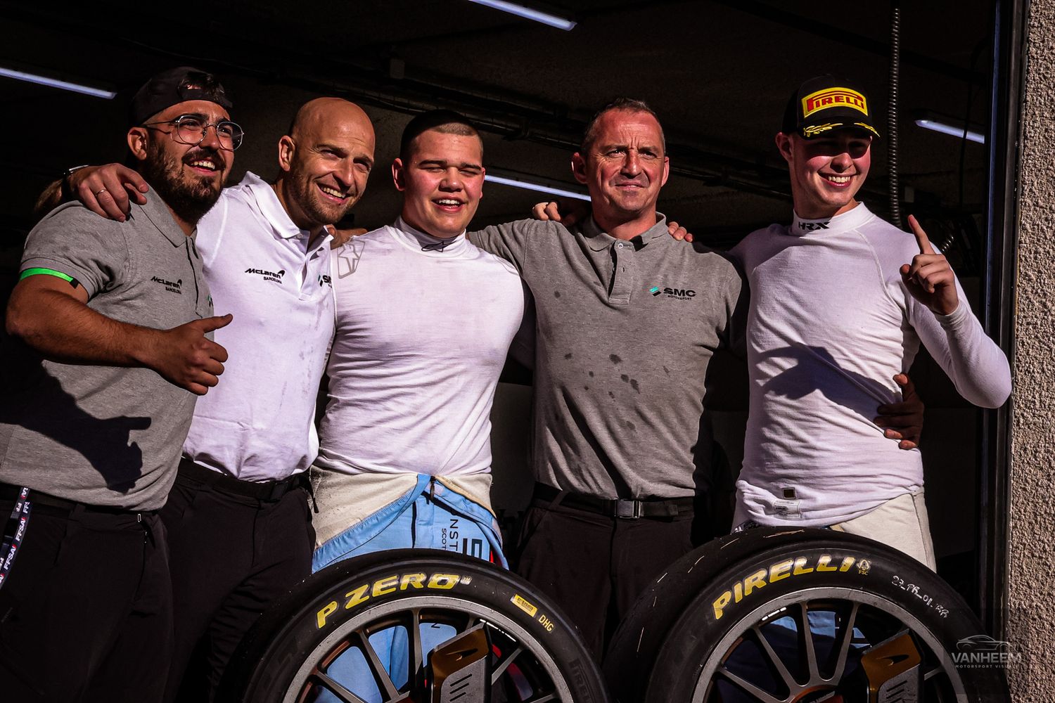 Racing team members pose together near a Pirelli tire display.