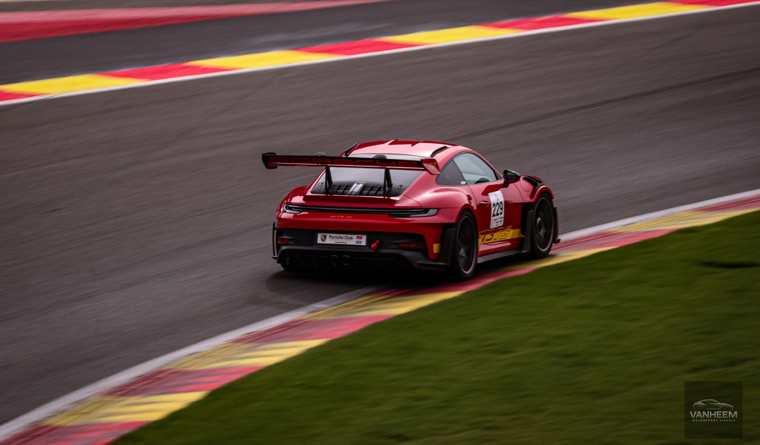 Red Porsche 911 GT3 race car speeding on Spa-Francorchamps circuit track.