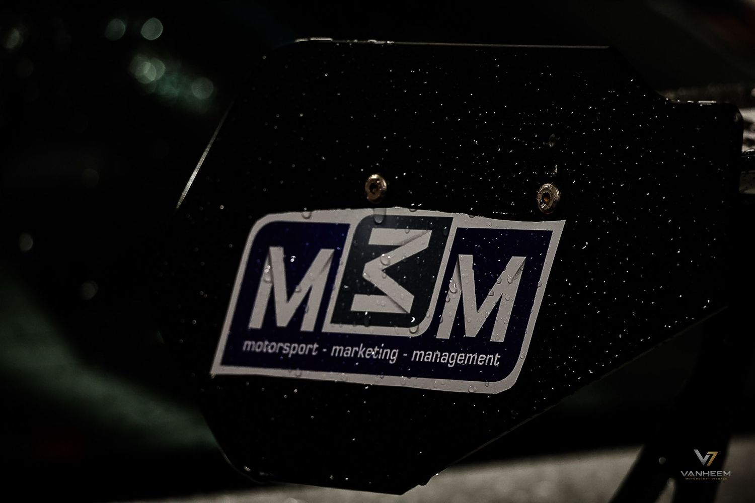 Close-up of MBM Motorsport Marketing Management logo on a dark racing car surface.