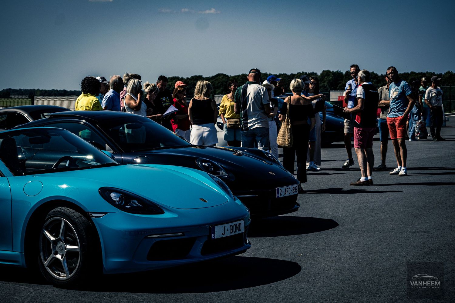 A row of blue McLaren supercars on display at an outdoor car show with spectators viewing the vehicles.