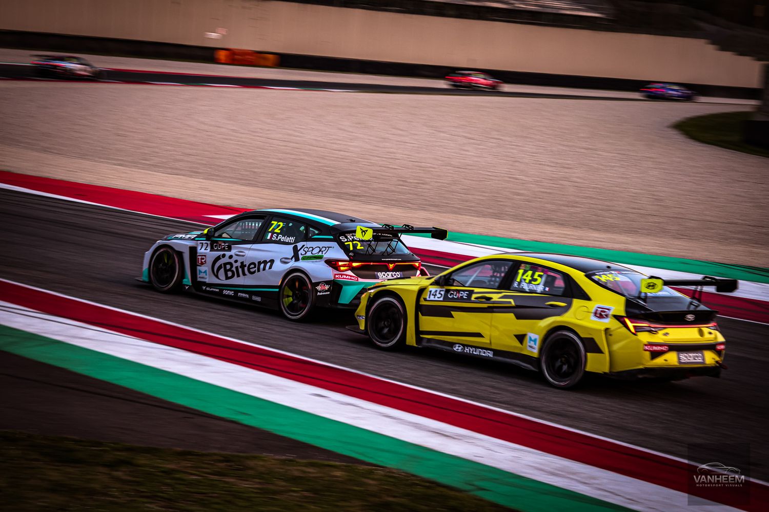 Racing cars compete on a colorful racetrack with red and green curbing during a motorsport competition.