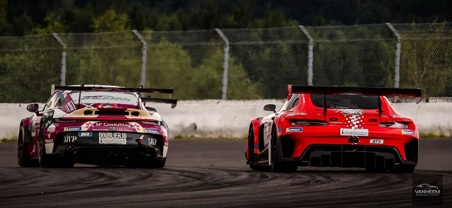 Two racing cars, a white Porsche and red Mercedes-AMG GT3, compete on a professional race track surrounded by trees.