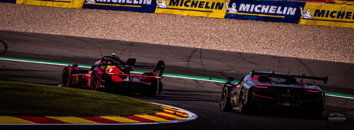 Two racing cars compete on a track with Michelin advertising boards in the background during a motorsport event.