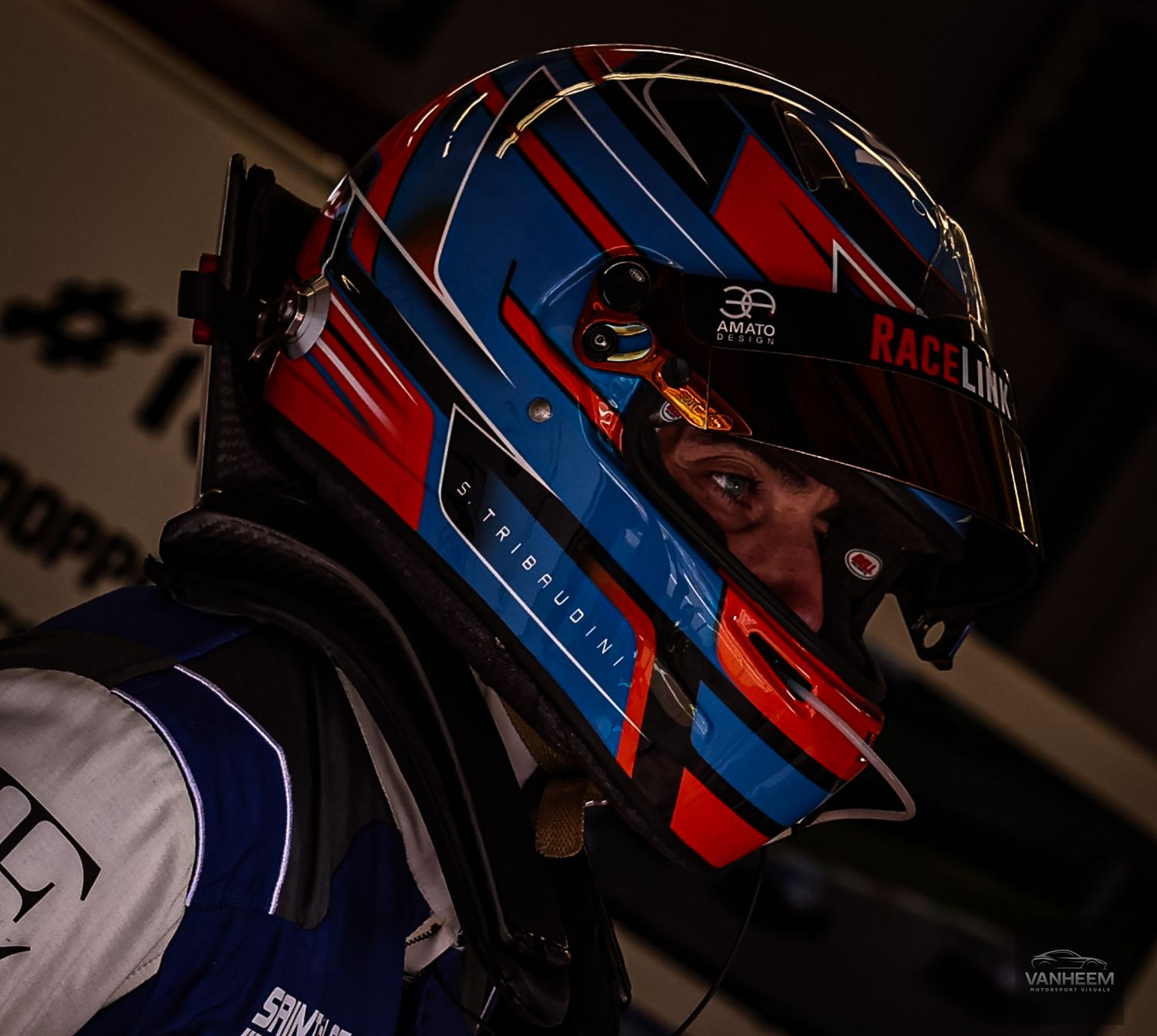 Racing driver wearing a red and blue helmet with black visor in low light conditions.