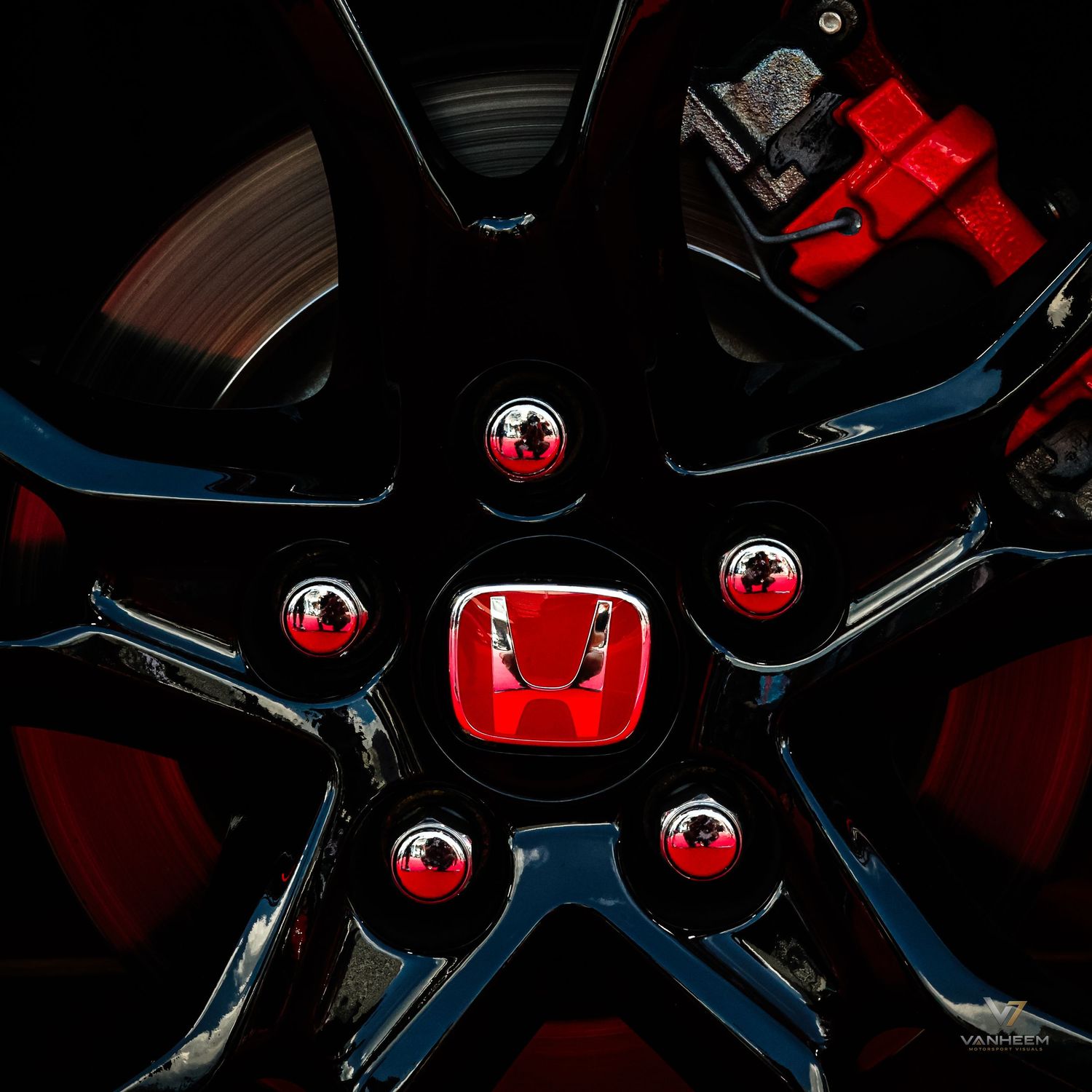 Close-up of a black Honda alloy wheel with red brake calipers and a red Honda logo center cap.