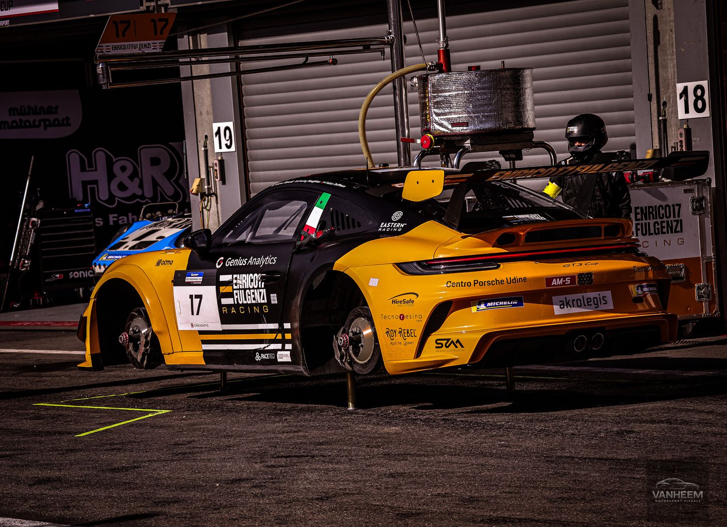Row of bright yellow racing cars lined up in pit lane at dusk.