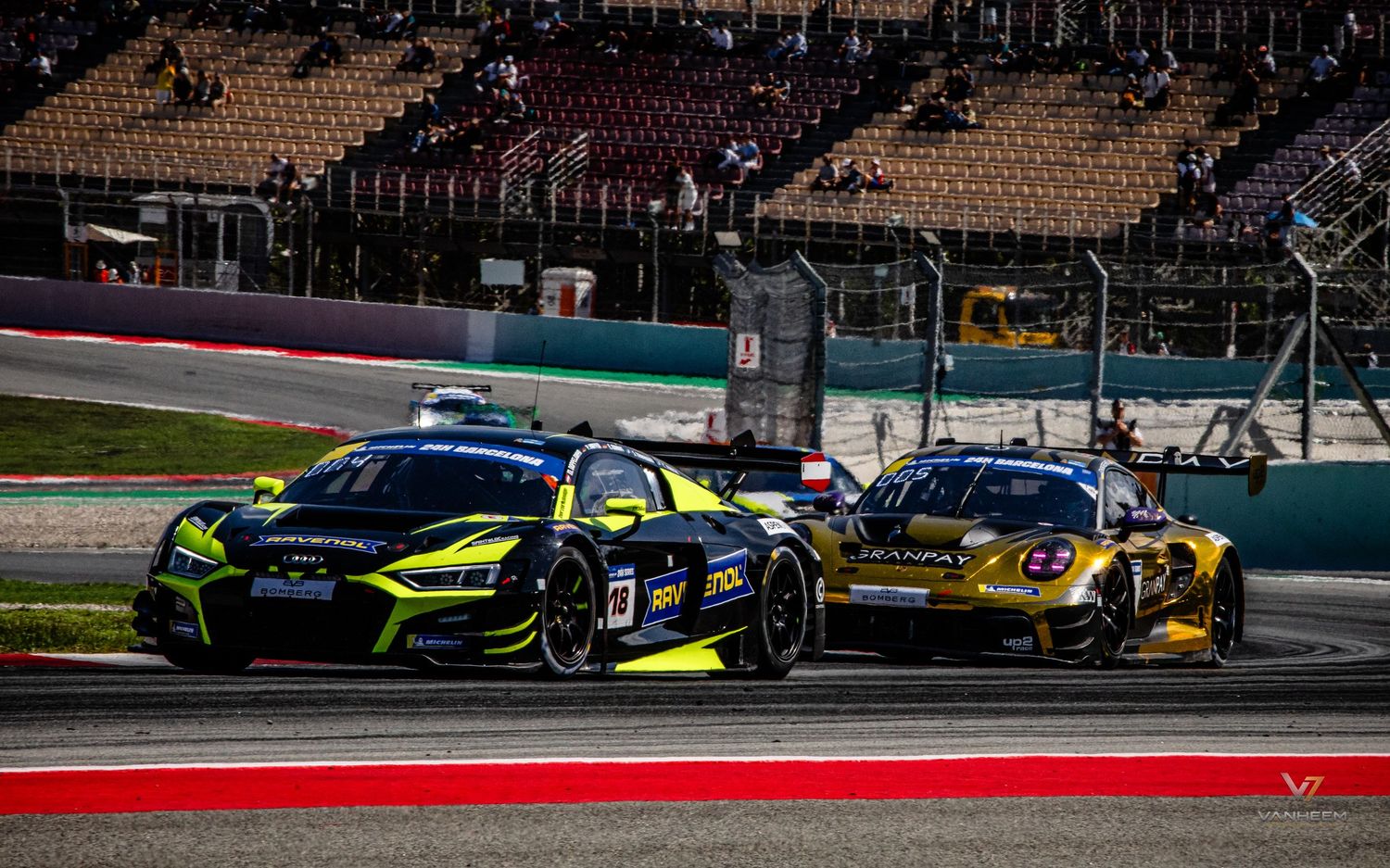 Two GT racing cars, a black Audi and yellow Corvette, battle side by side on a motorsport circuit.