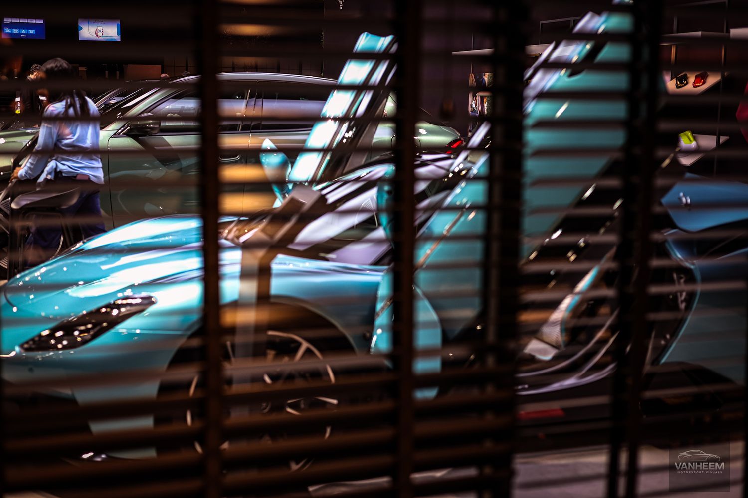 Futuristic car silhouettes viewed through venetian blinds creating dramatic striped lighting effects.