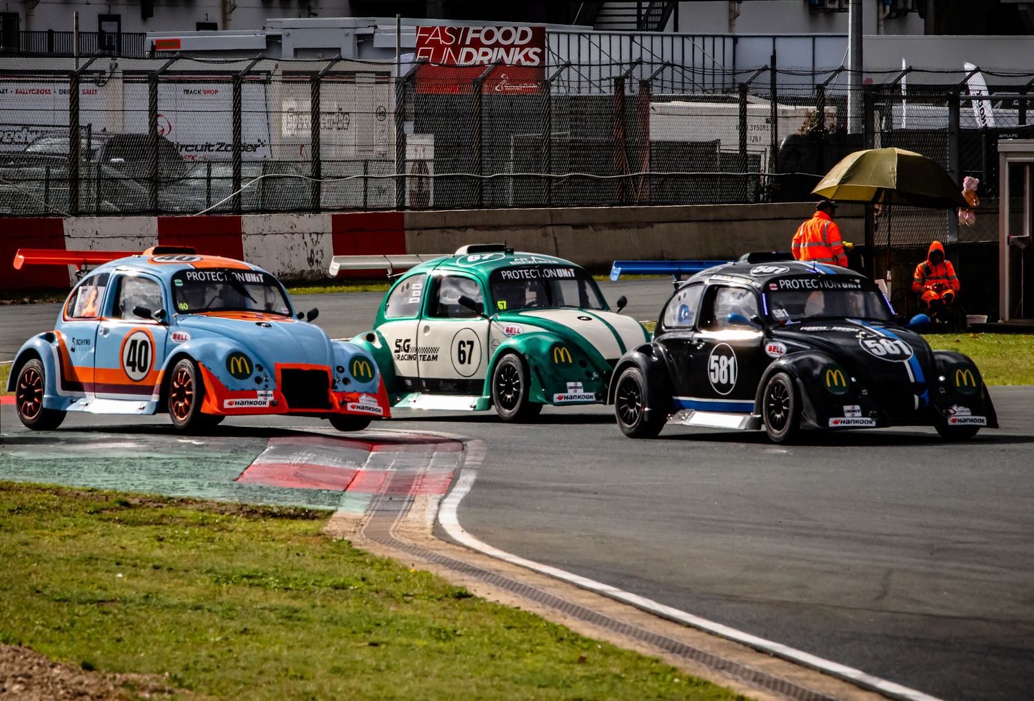 Three vintage racing cars compete on a circuit track, featuring Gulf livery and McDonald's sponsorship during a motorsport event.