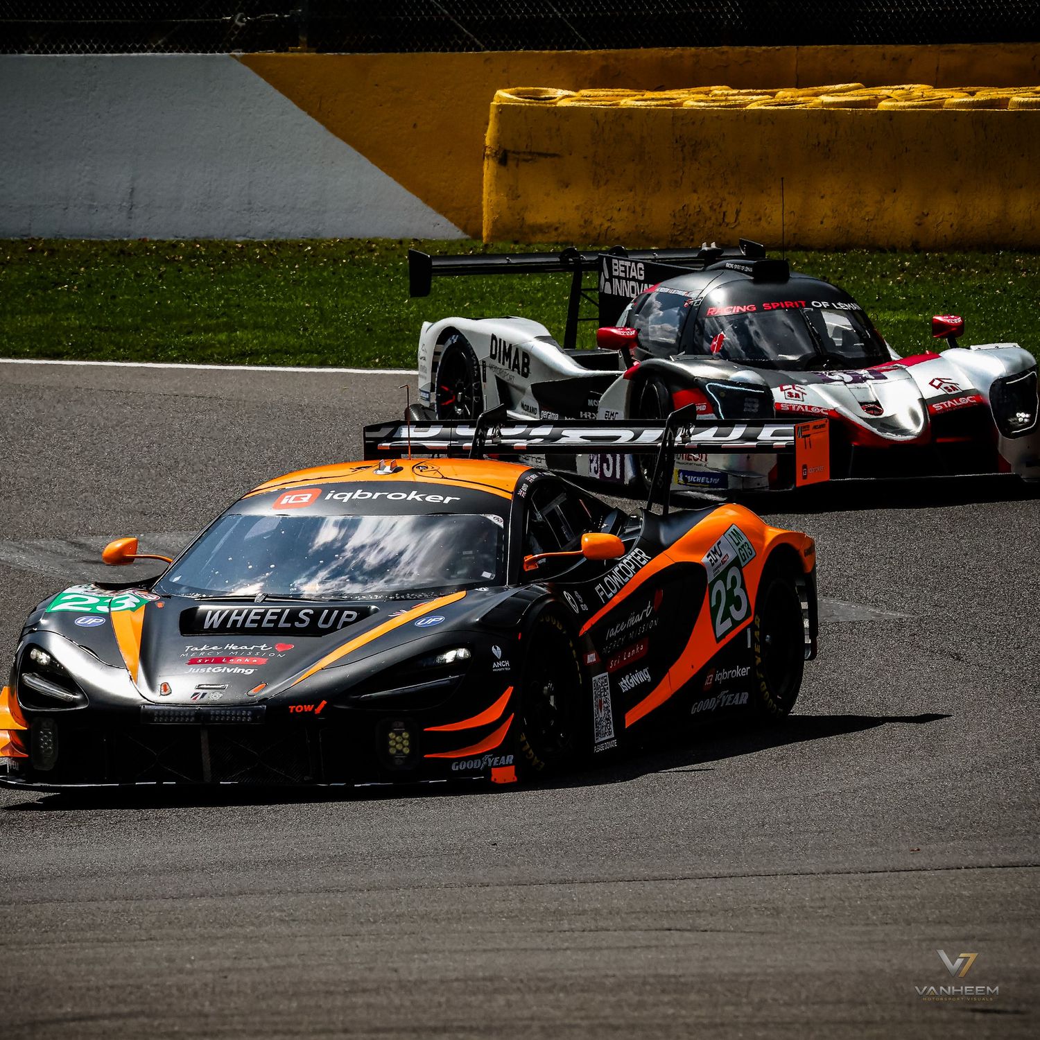 McLaren GT3 race car #29 in orange and black livery leads a pack of racing cars on a circuit track.