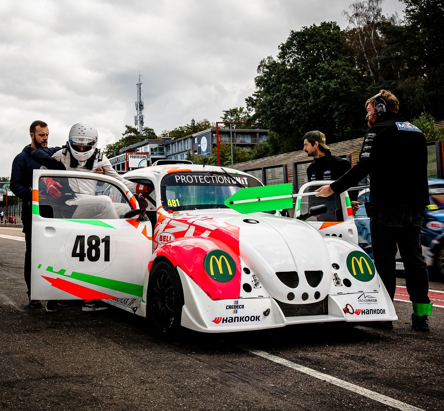 Race car #481 with McDonald's sponsorship in pit lane, crew preparing white and red vehicle at motorsport circuit.