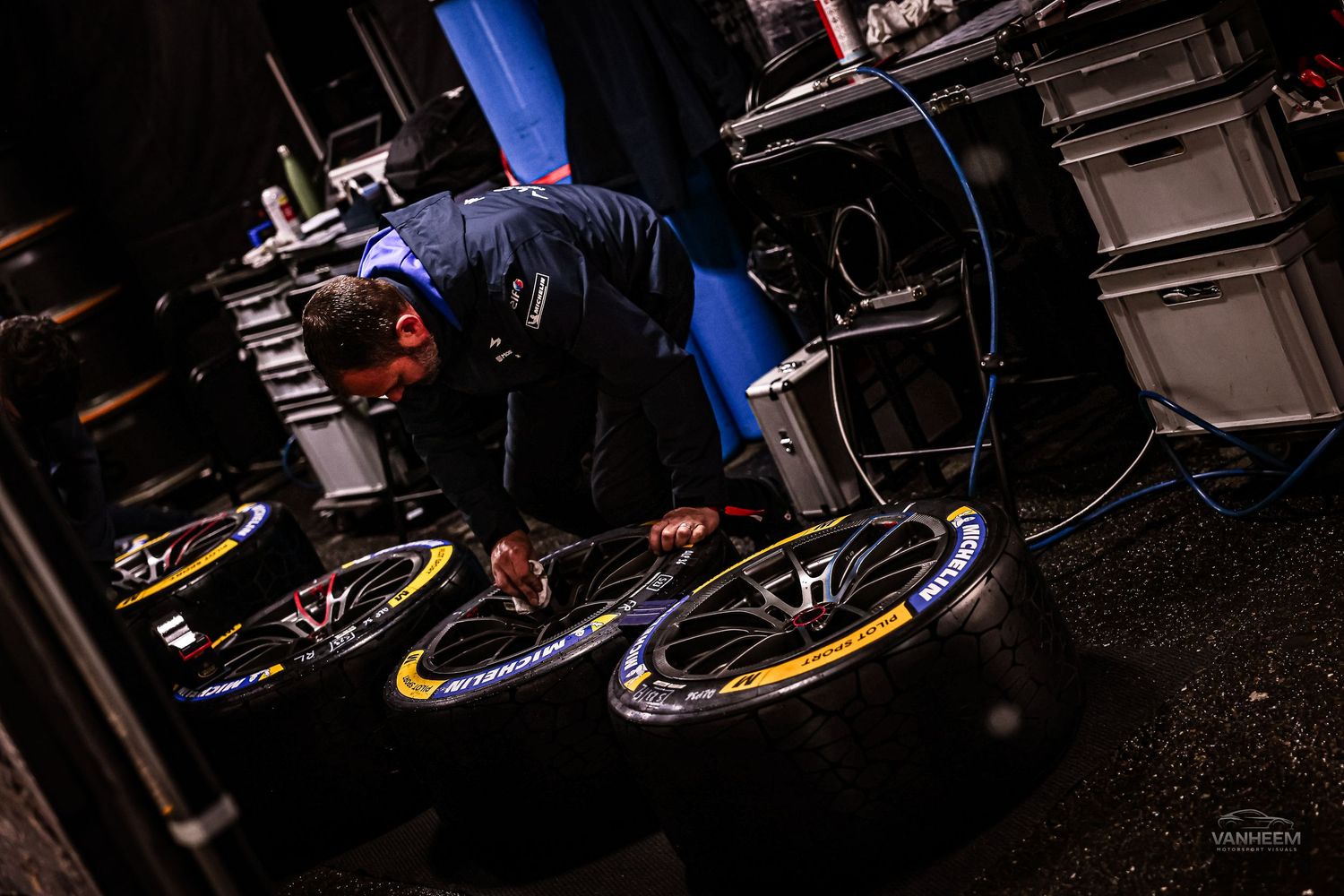 F1 mechanic inspecting Pirelli racing tires in a dimly lit pit garage during a Formula One race event.