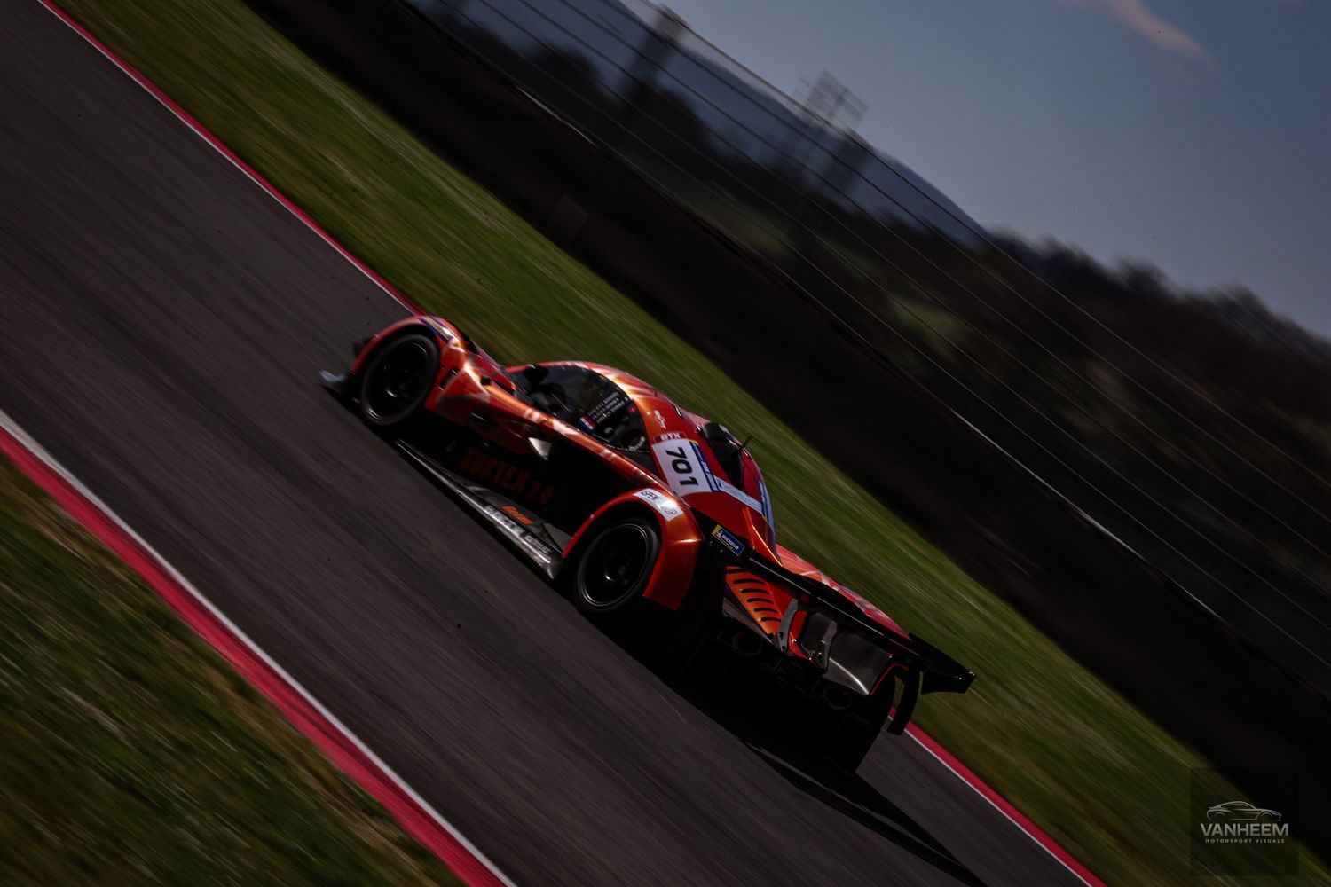 Formula 1 race car speeds along a race track with green grass and dark skies in the background.