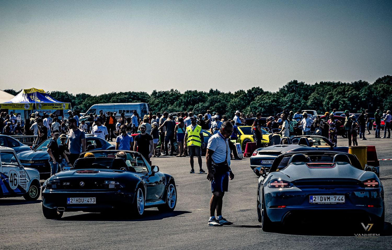 Sports cars lined up at an outdoor racing event with a crowd of spectators gathered on a sunny day.
