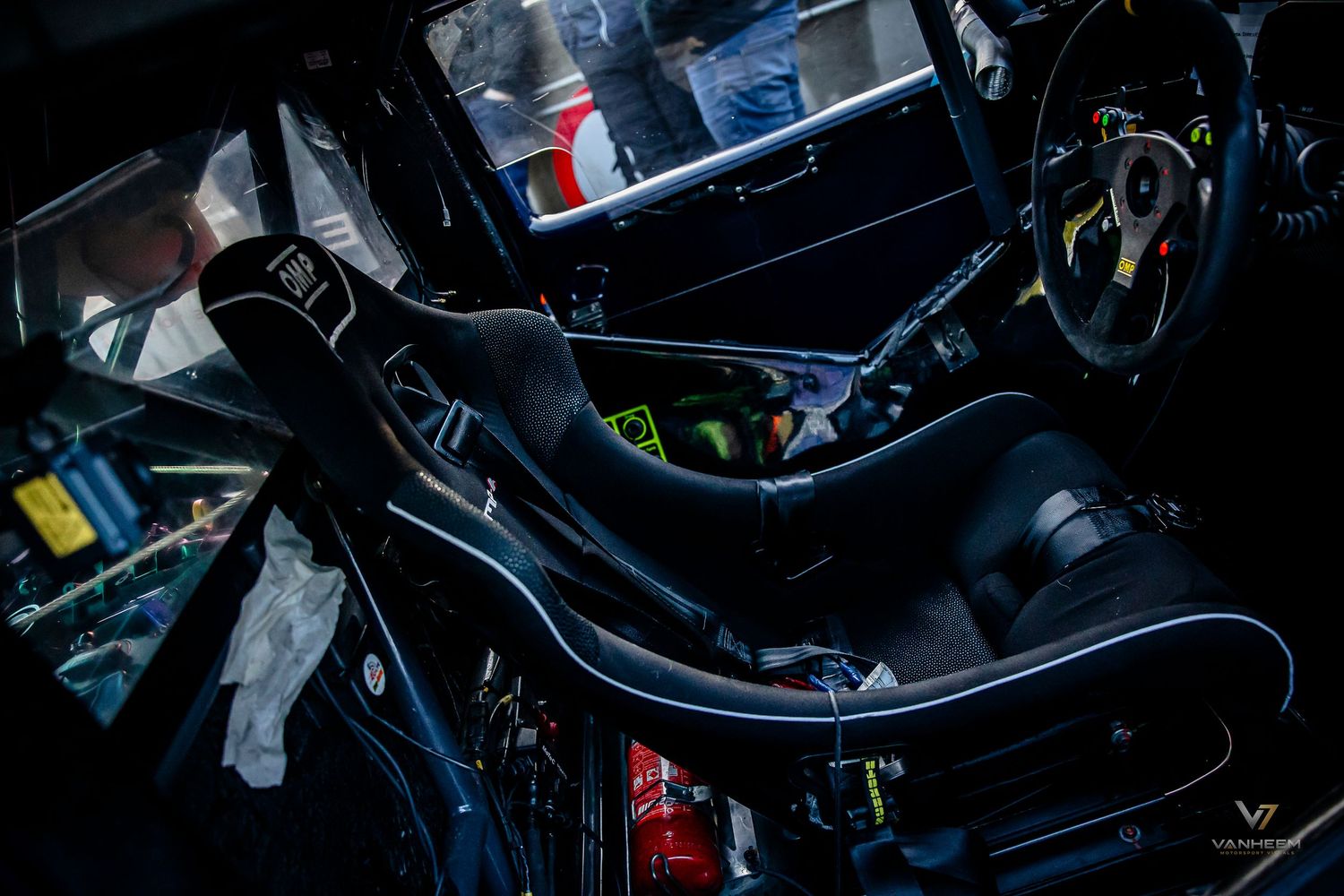 Interior view of a high-performance race car featuring a black racing seat, roll cage, and yellow steering wheel.