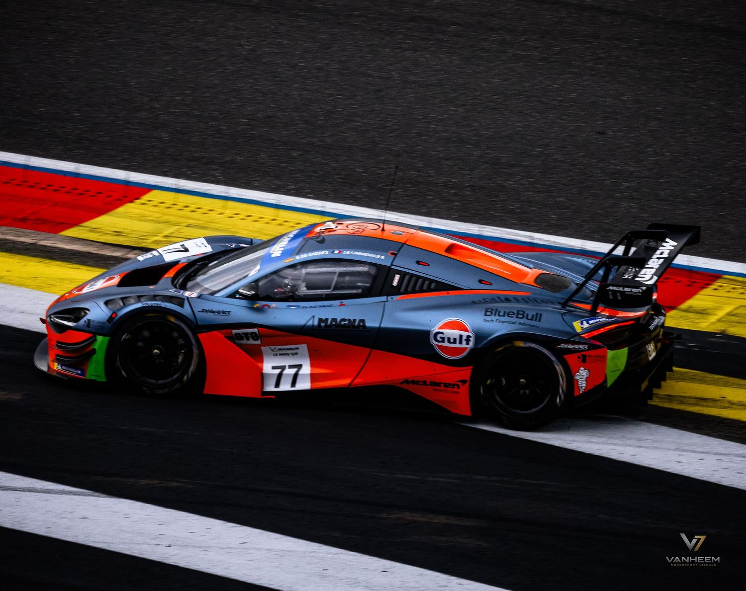Gulf-liveried #77 racing car speeding on track at motorsport event, featuring orange, blue, and red livery.