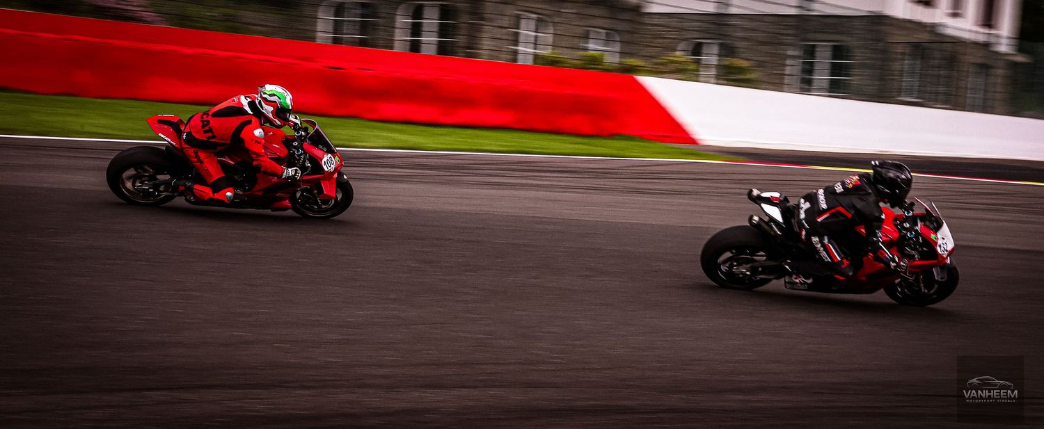 Two red motorcycles racing on a track with motion blur background, capturing high-speed action on a circuit.