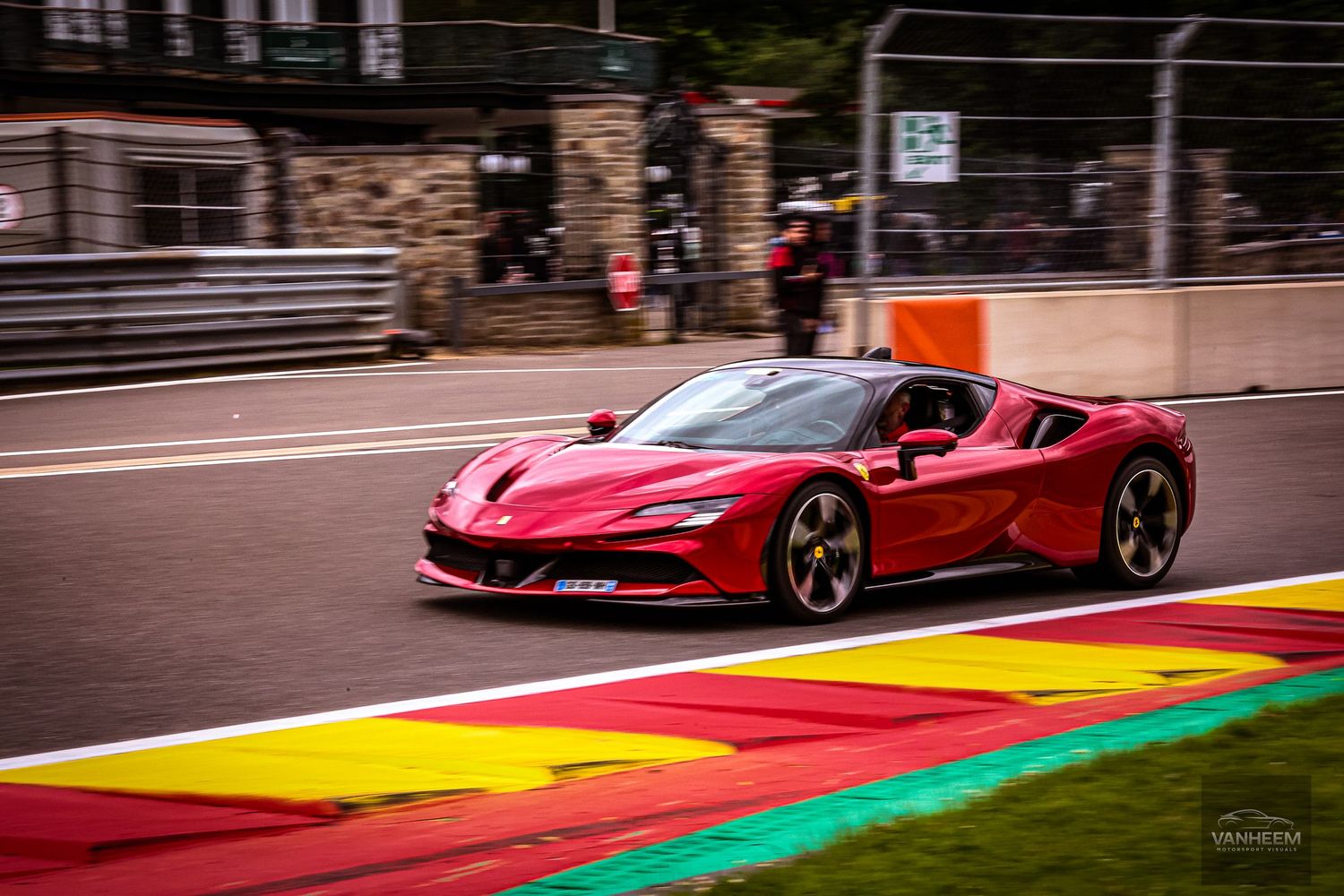 Red Ferrari SF90 Stradale supercar on a colorful race track circuit, likely Spa-Francorchamps, Belgium.
