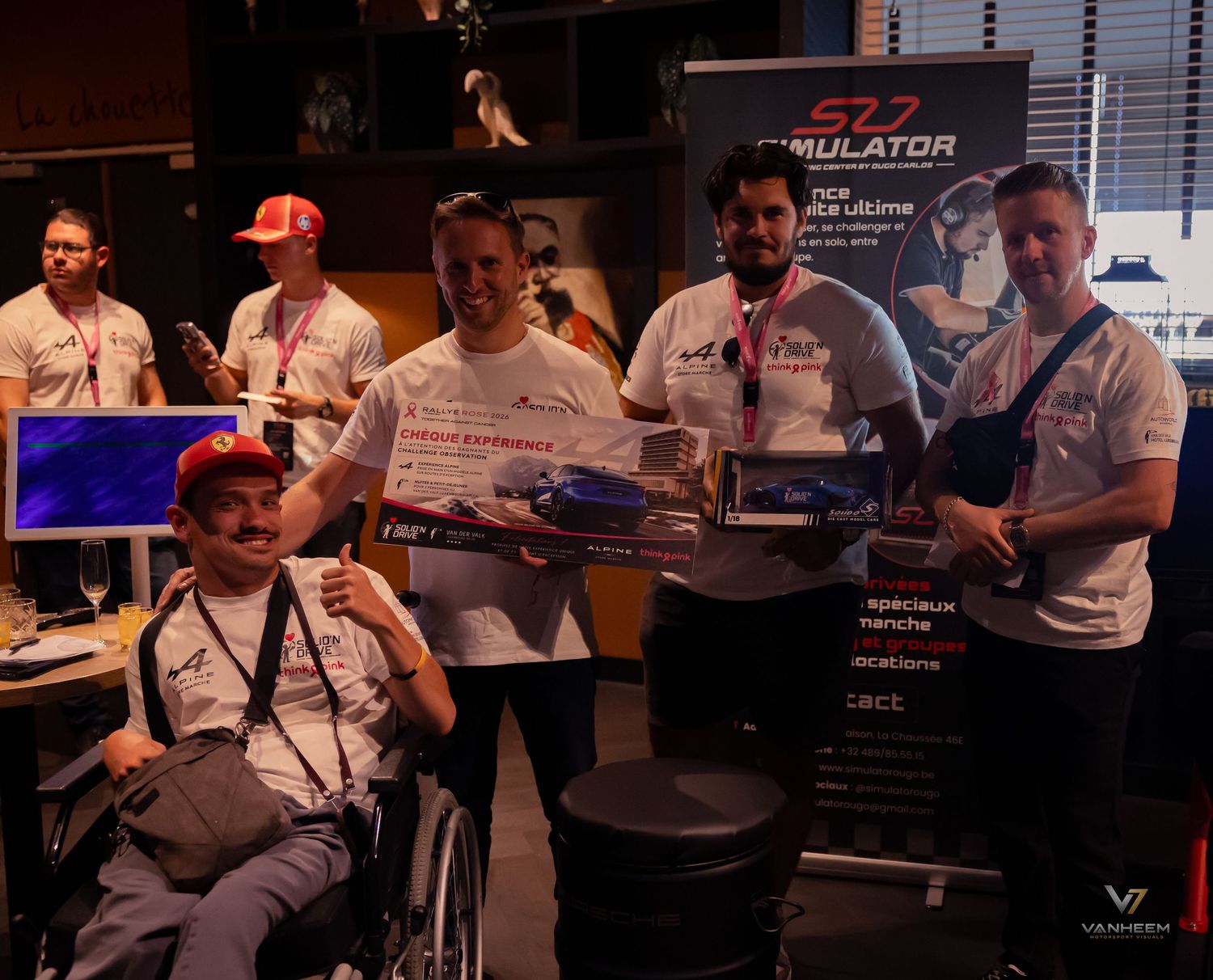 Group of people posing with awards at an SZP Simulator gaming event, including a wheelchair user holding a prize.