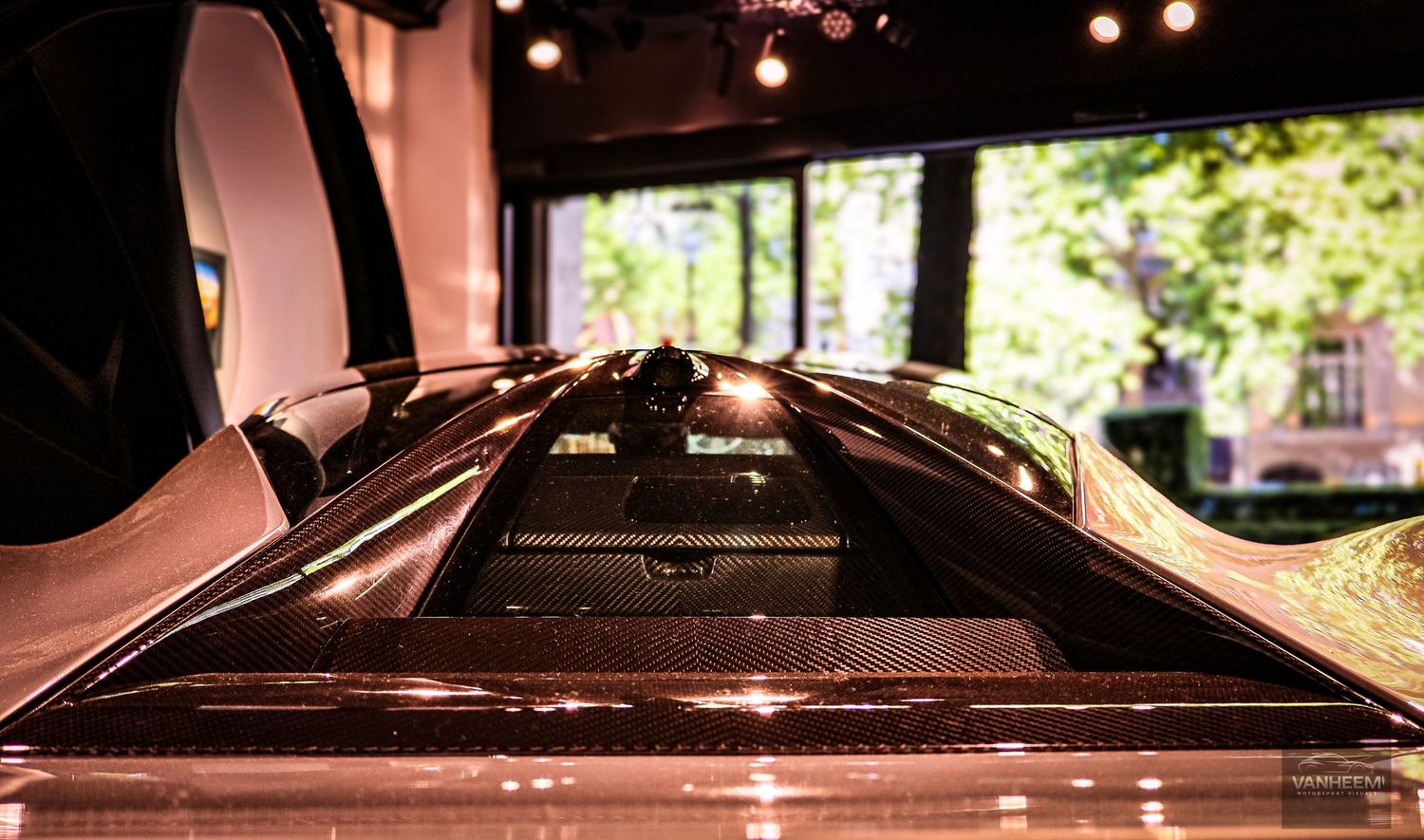 Close-up view of a luxury supercar carbon fiber engine cover with glossy reflections in an elegant showroom setting.