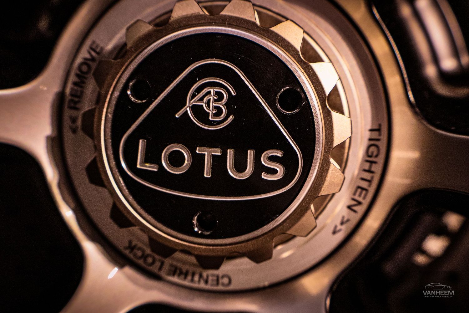 Close-up of a Lotus car wheel center cap featuring the iconic Lotus logo on a dark metallic background.