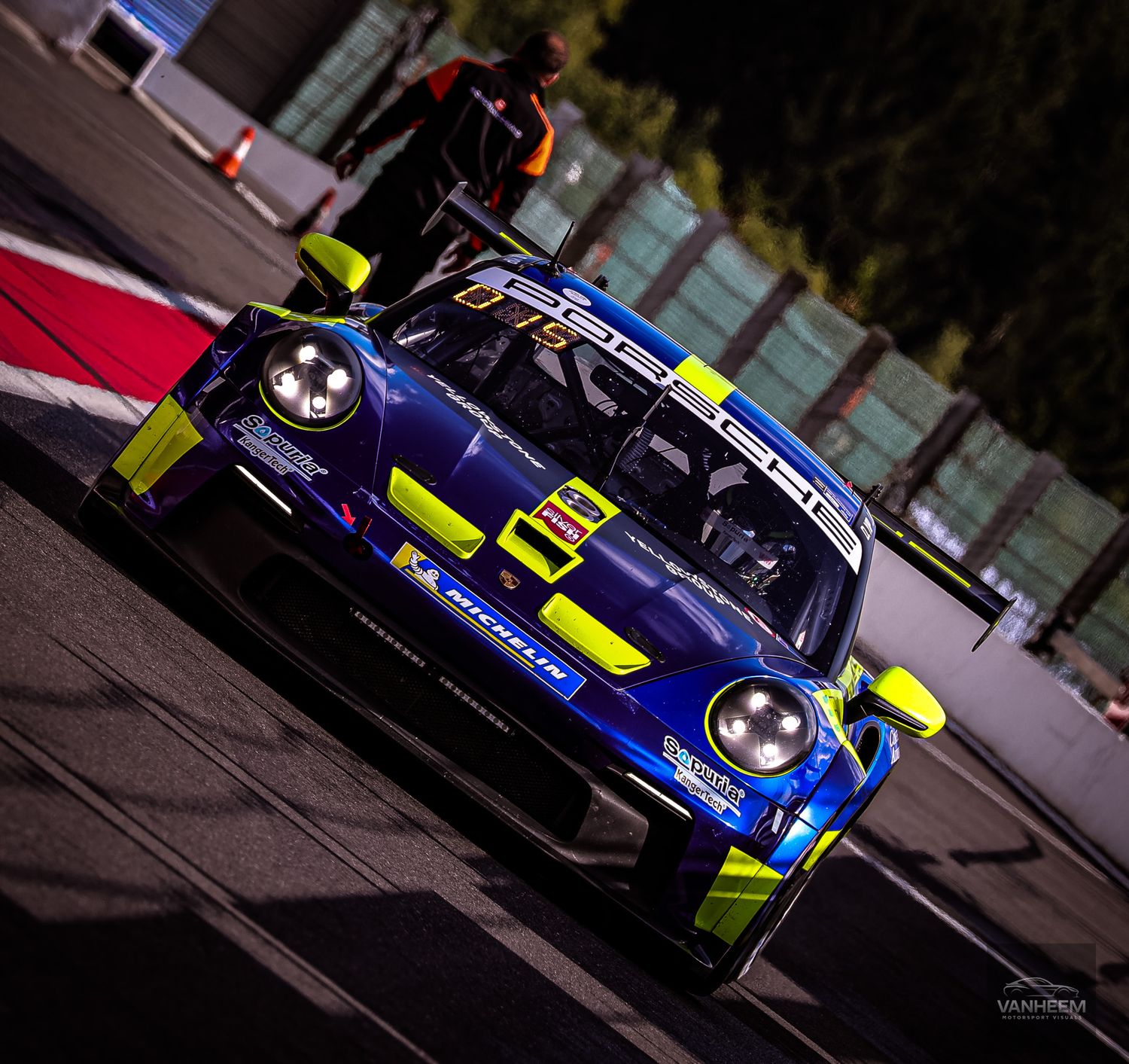 Blue and yellow Porsche 911 GT3 racing car speeding on track during a motorsport competition event.