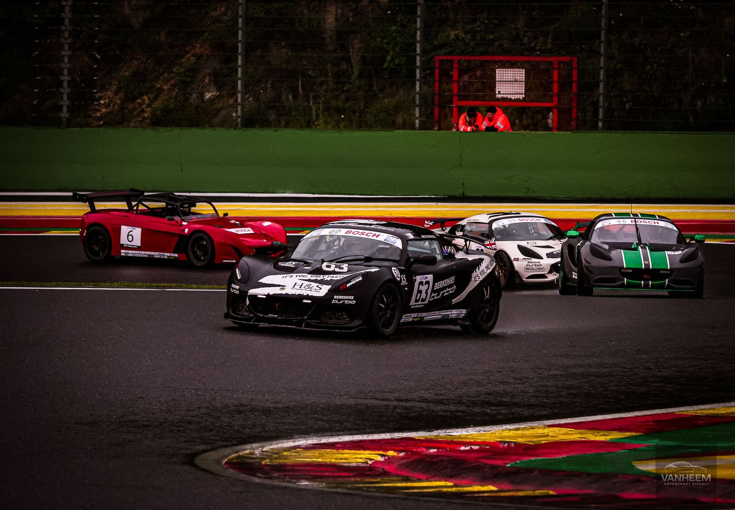 Racing cars compete on a wet track at Spa-Francorchamps circuit, led by a black sports car during an intense race.