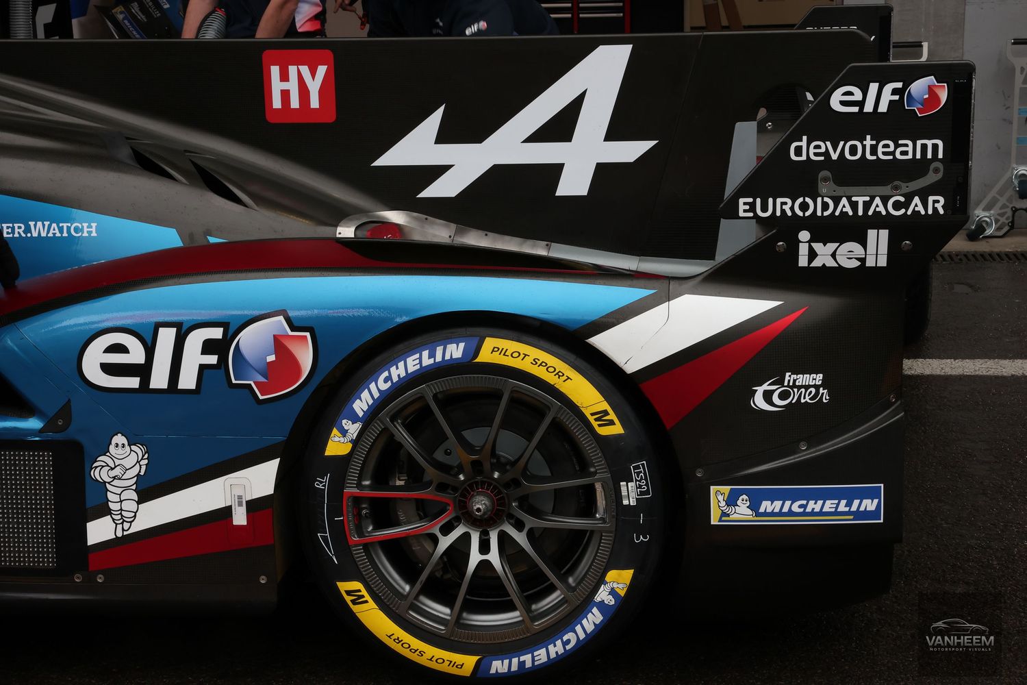 Alpine A470 LMP2 race car detail showing Elf, Michelin sponsorship logos and yellow-rimmed tire at Le Mans.