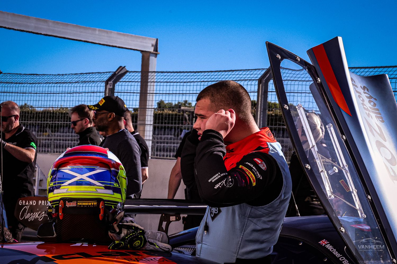 Racing pit crew members work on cars in garage bays during a motorsport event.