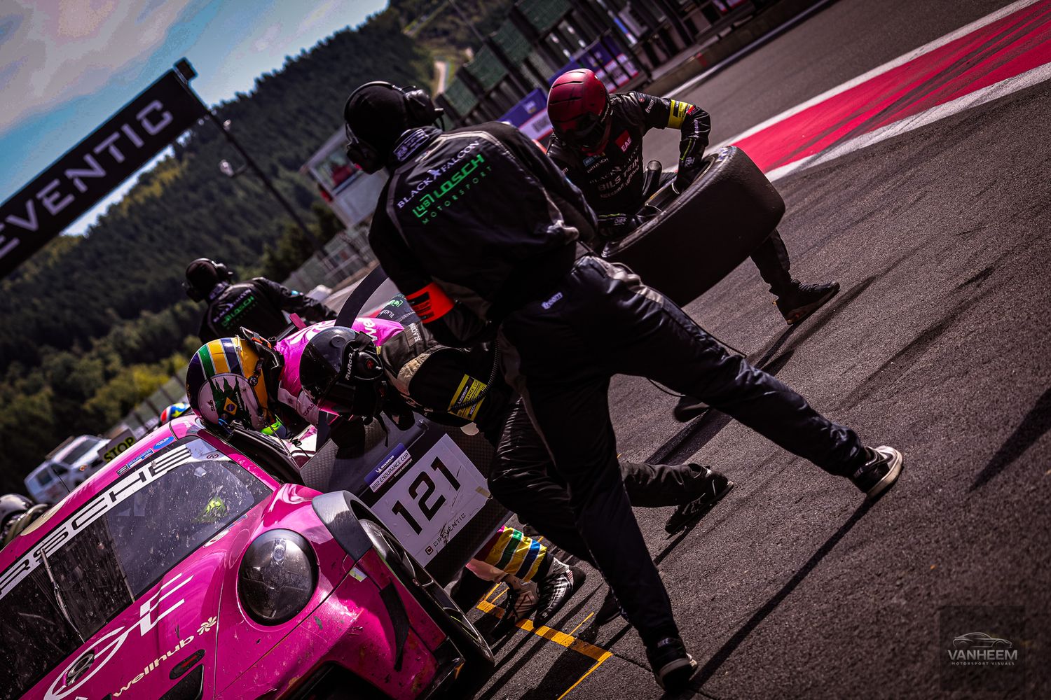Pink and black race cars lined up on track during sunset at a motorsport competition.