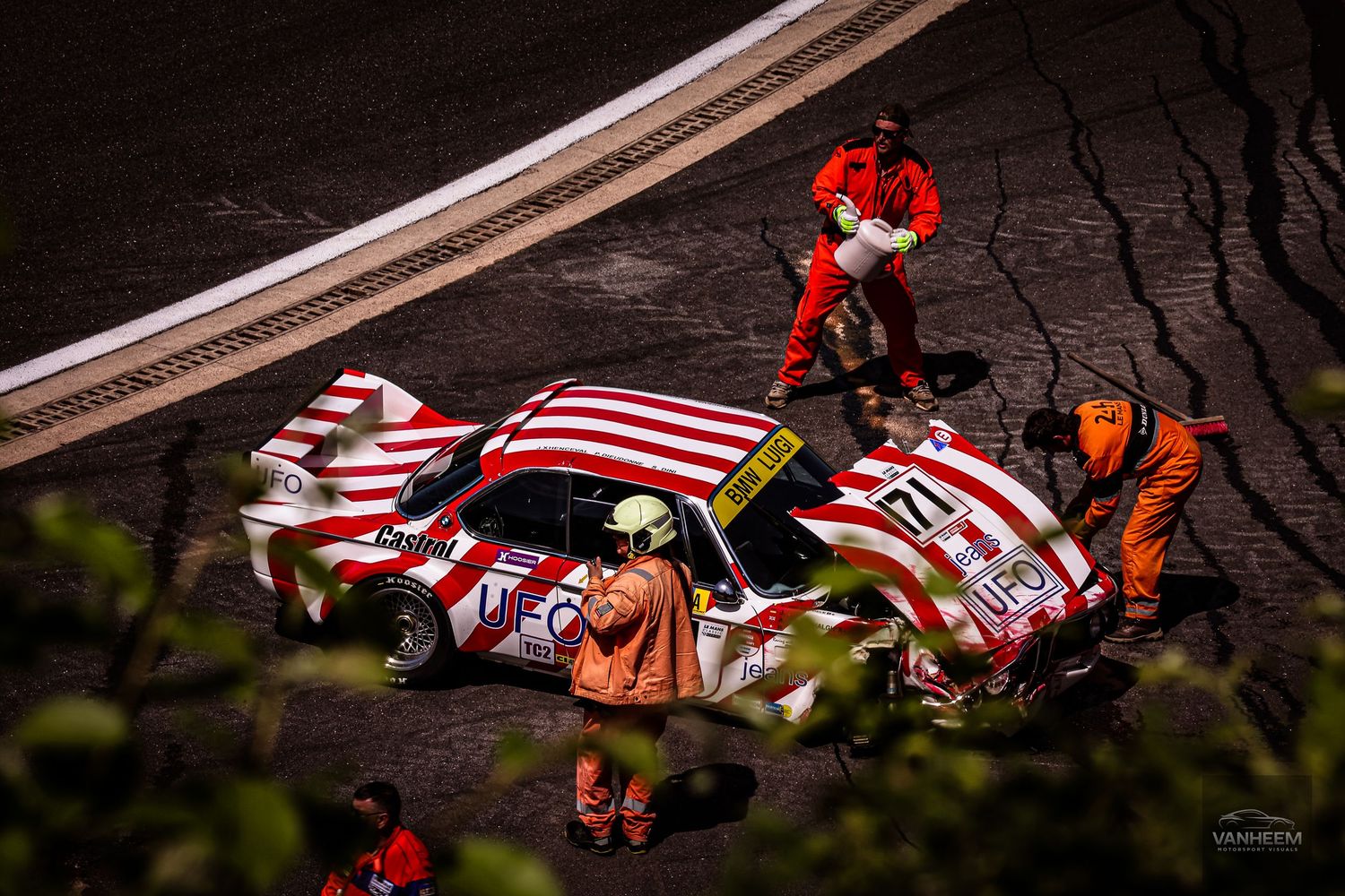 A red and white race car surrounded by crew members in safety gear during a nighttime pit stop on a racing circuit.