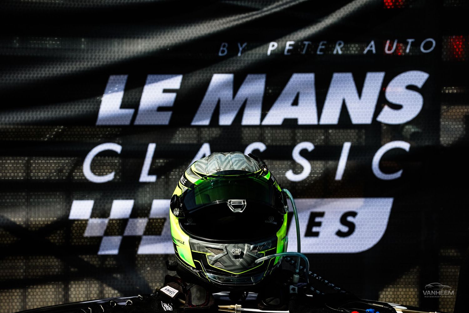 Racing helmet displayed in front of Le Mans Classic Series banner by Peter Auto at motorsport event.