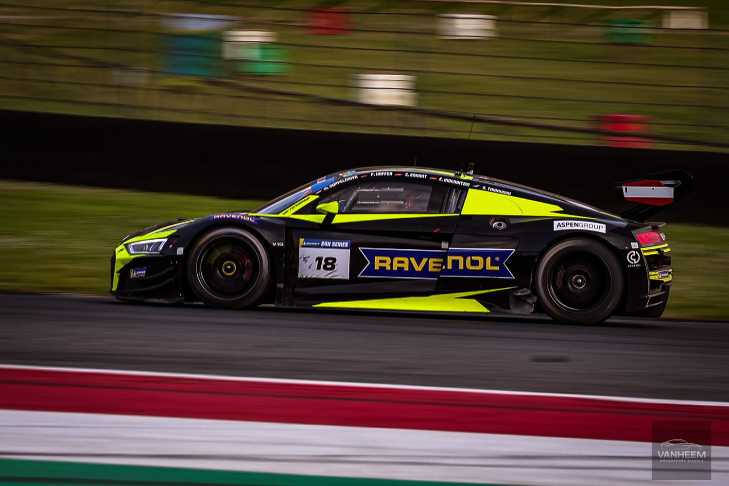 Race cars speed around a track during a competitive motorsport event at dusk with colorful lighting.
