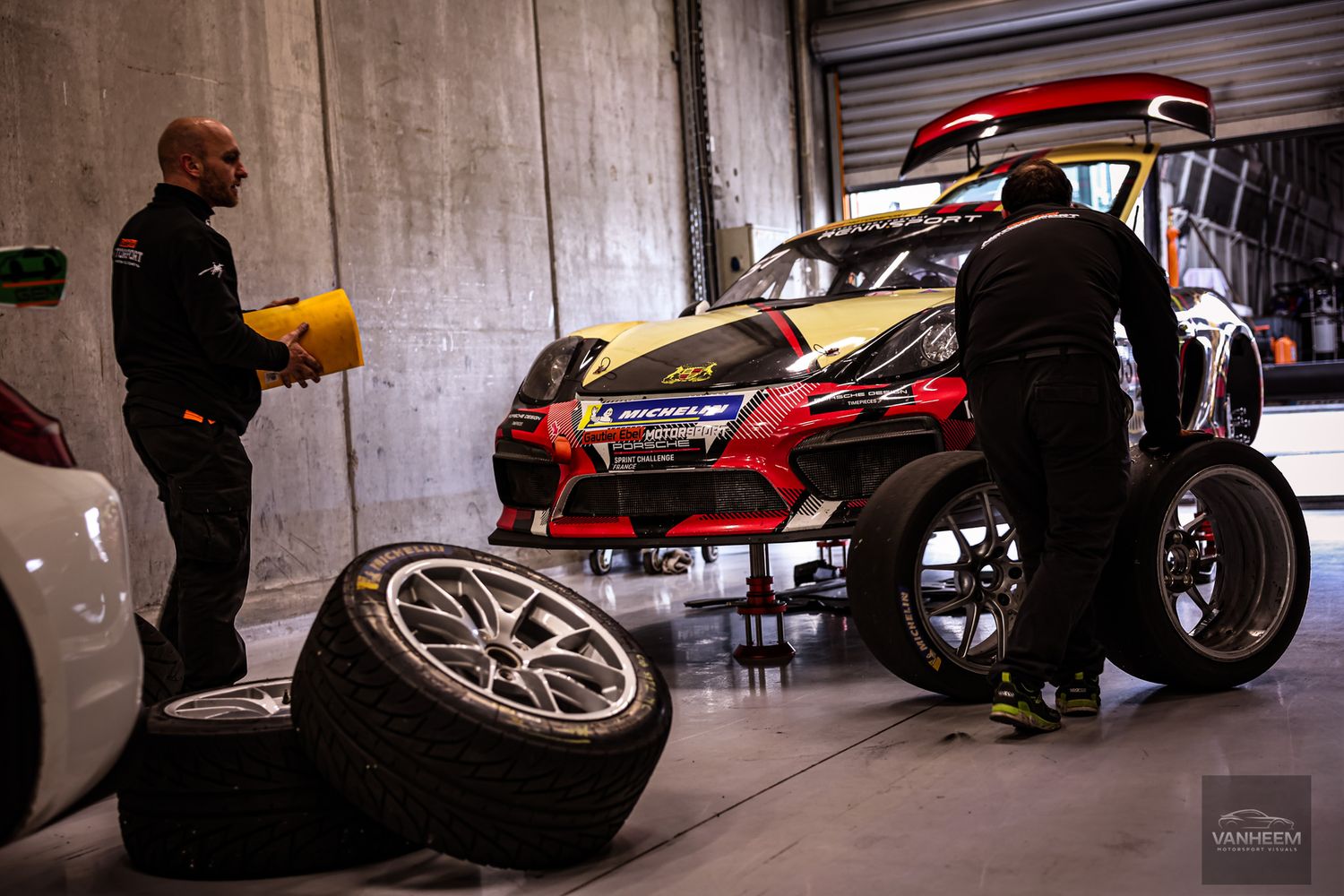 Racing team mechanics changing tires on a rally car in a garage pit stop during a motorsport event.