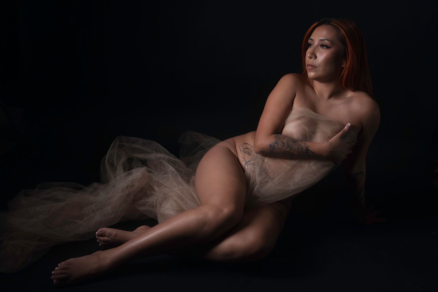 Tattooed woman reclining in sheer tulle wrap, fine art nude boudoir photography Fort Worth by Lock & Key Photography.