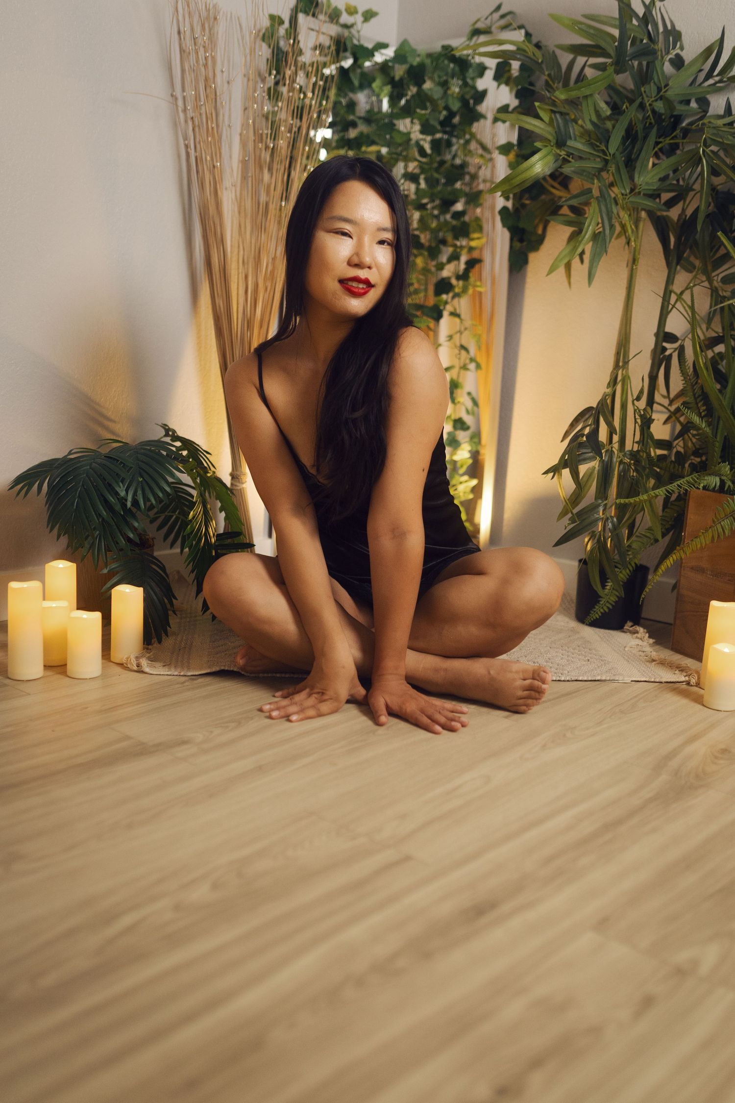 Boudoir Photography Fort Worth, Texas- woman in black lingerie kneeling on floor with candlelight and greenery backdrop.