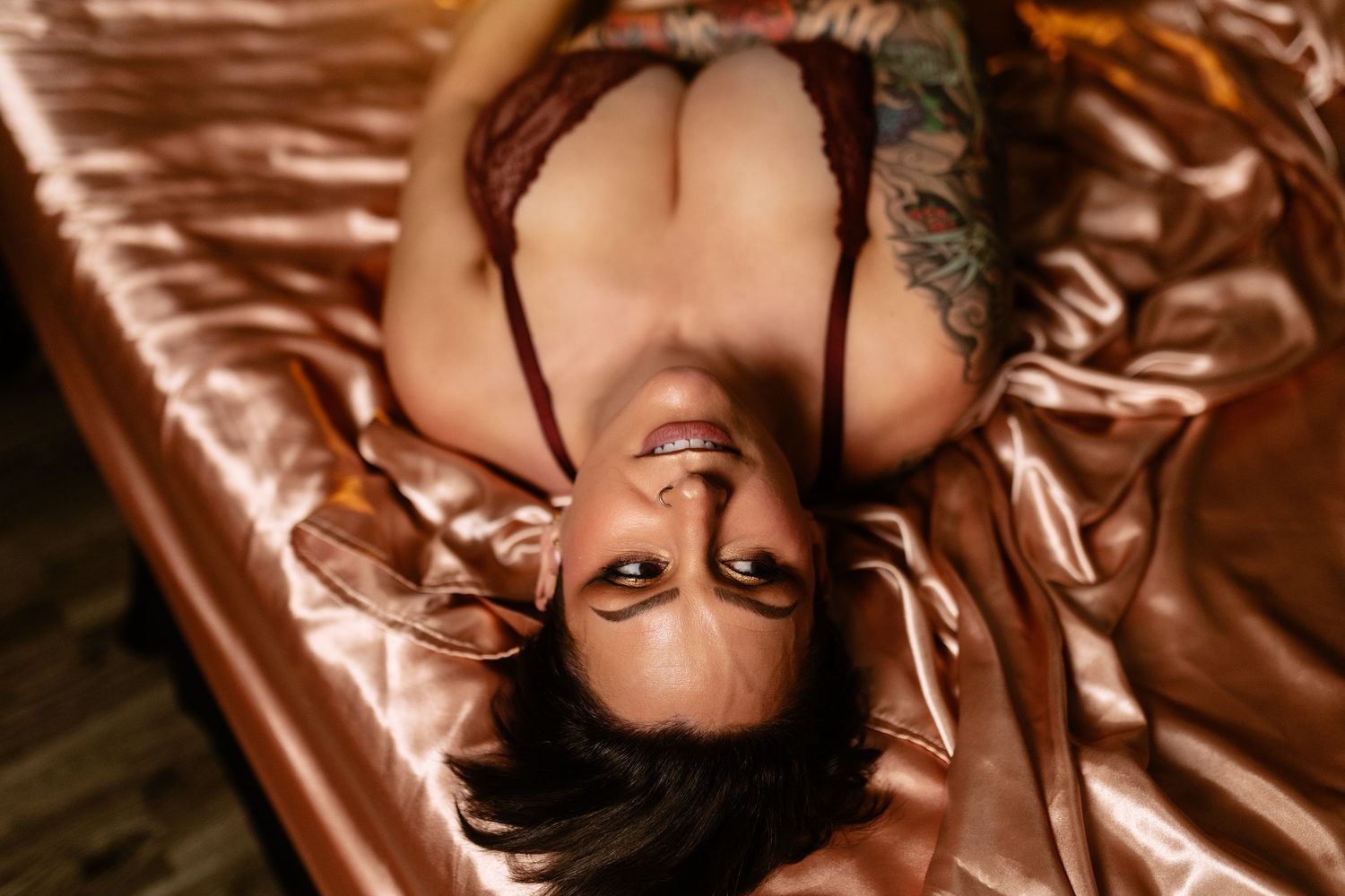 Woman lying back on rose gold satin, luxury boudoir portrait serving Dallas, TX.