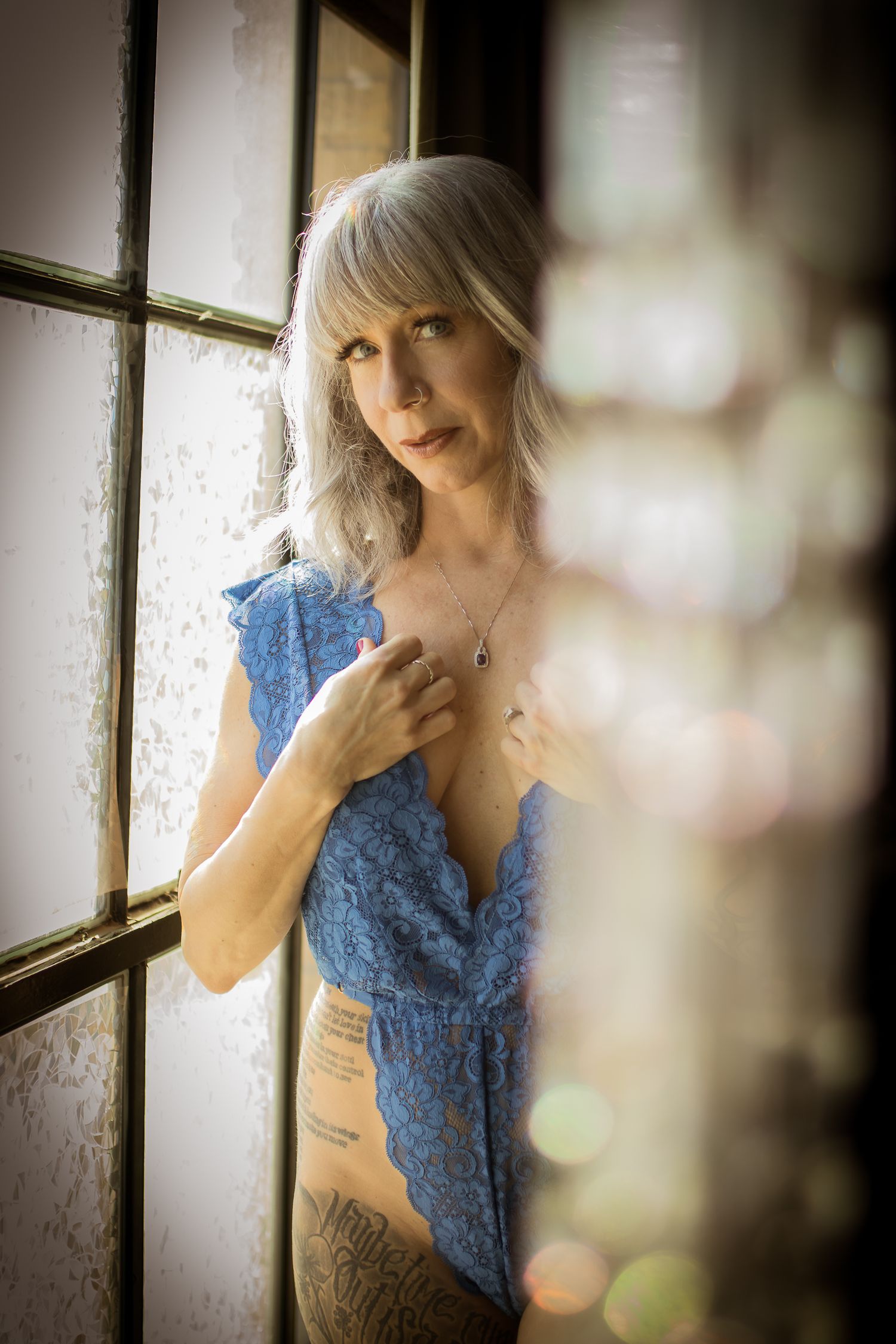 Woman over 50 in blue lingerie standing by window in natural light— Fort Worth boudoir studio Lock & Key