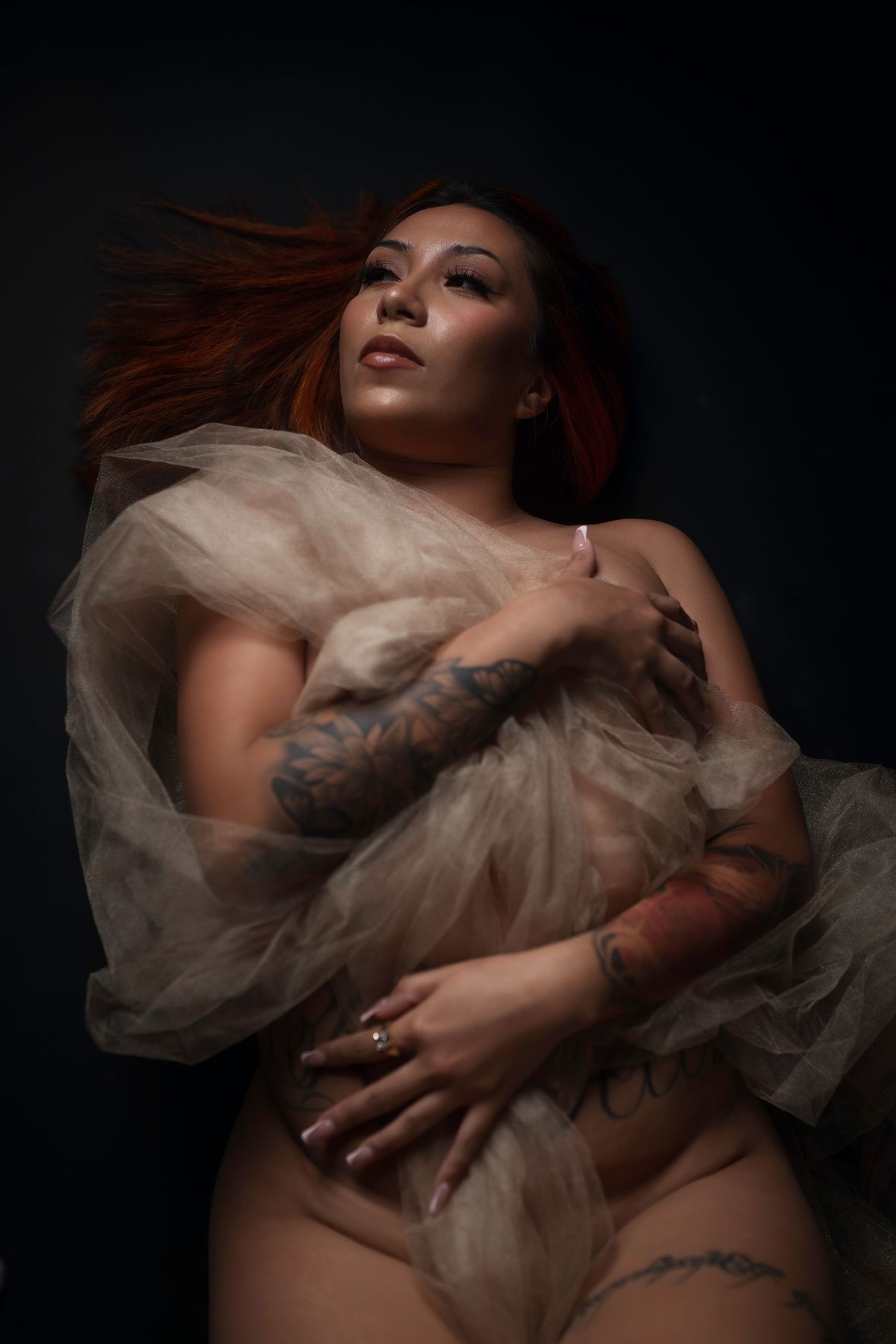 Moody boudoir portrait wrapped in sheer fabric, painterly single-source lighting, Fort Worth.