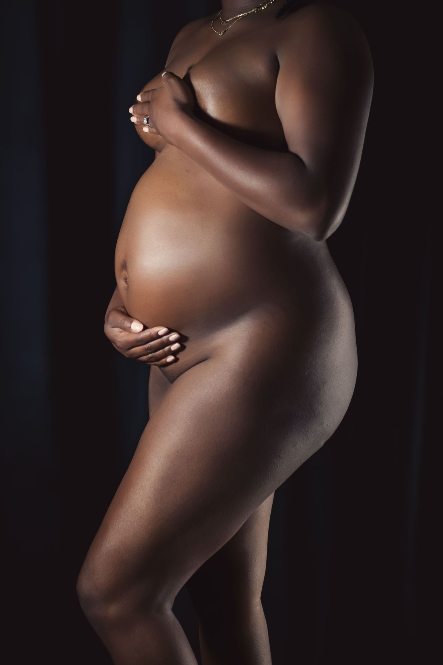 Pregnant black woman cradling bare bump in a maternity boudoir session — maternity boudoir photography DFW.