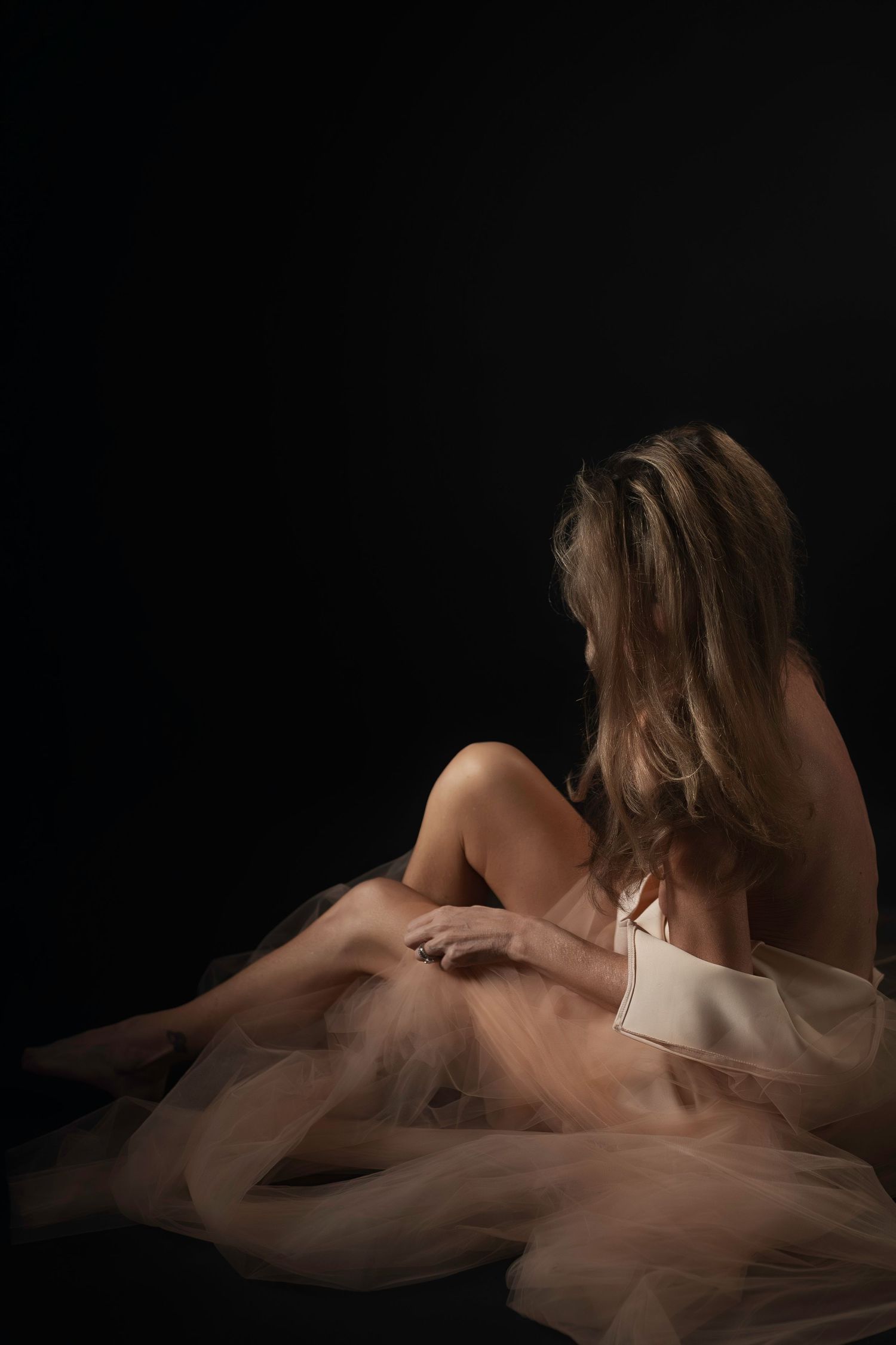 Fort Worth boudoir photographer, Lock & Key Photography, captures woman in dramatic lighting in a dress surrounded by blush tulle.