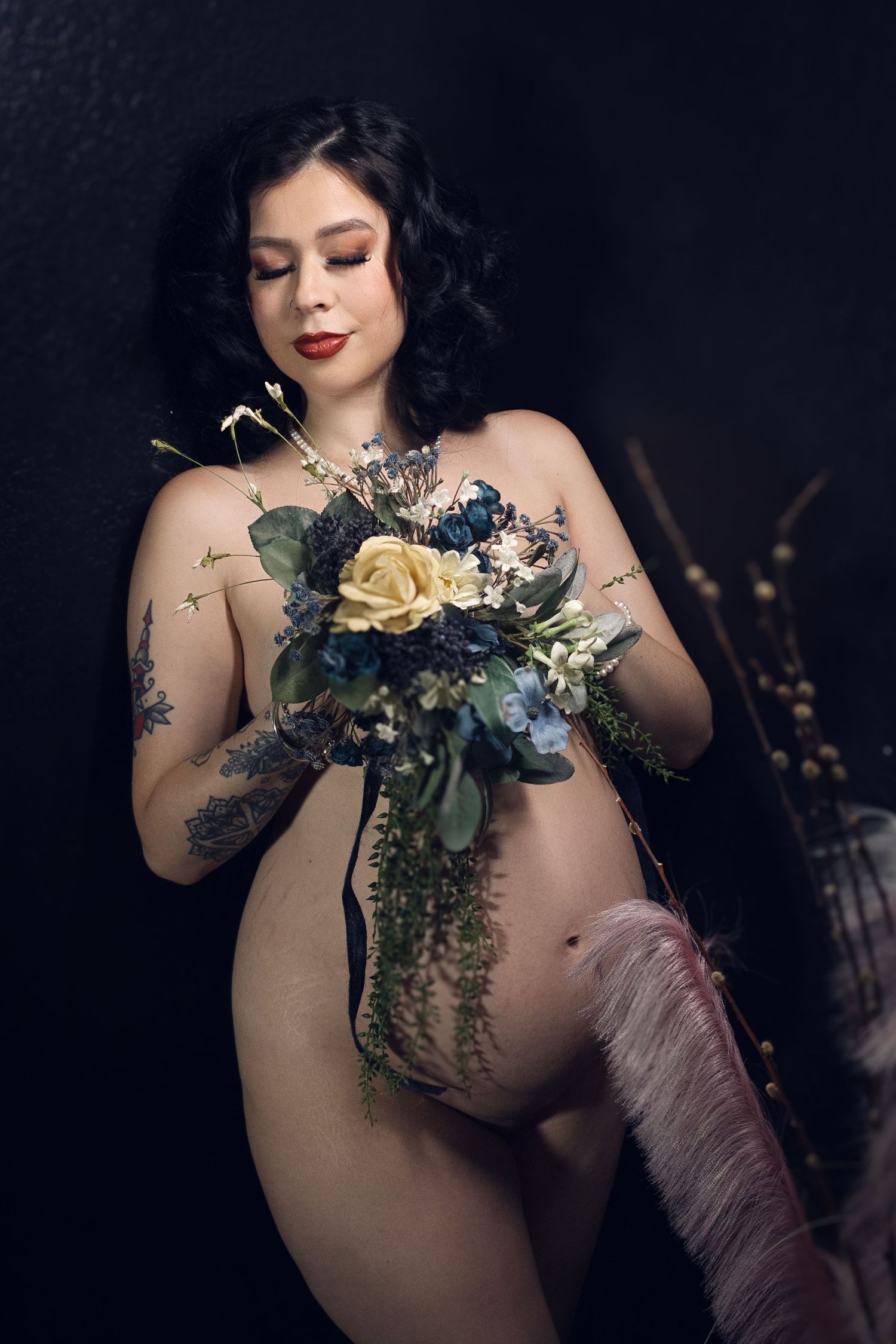 Pregnant woman holding flowers and draped in blue lace in a dark intimate maternity boudoir photo— Dallas Fort Worth Maternity Boudoir