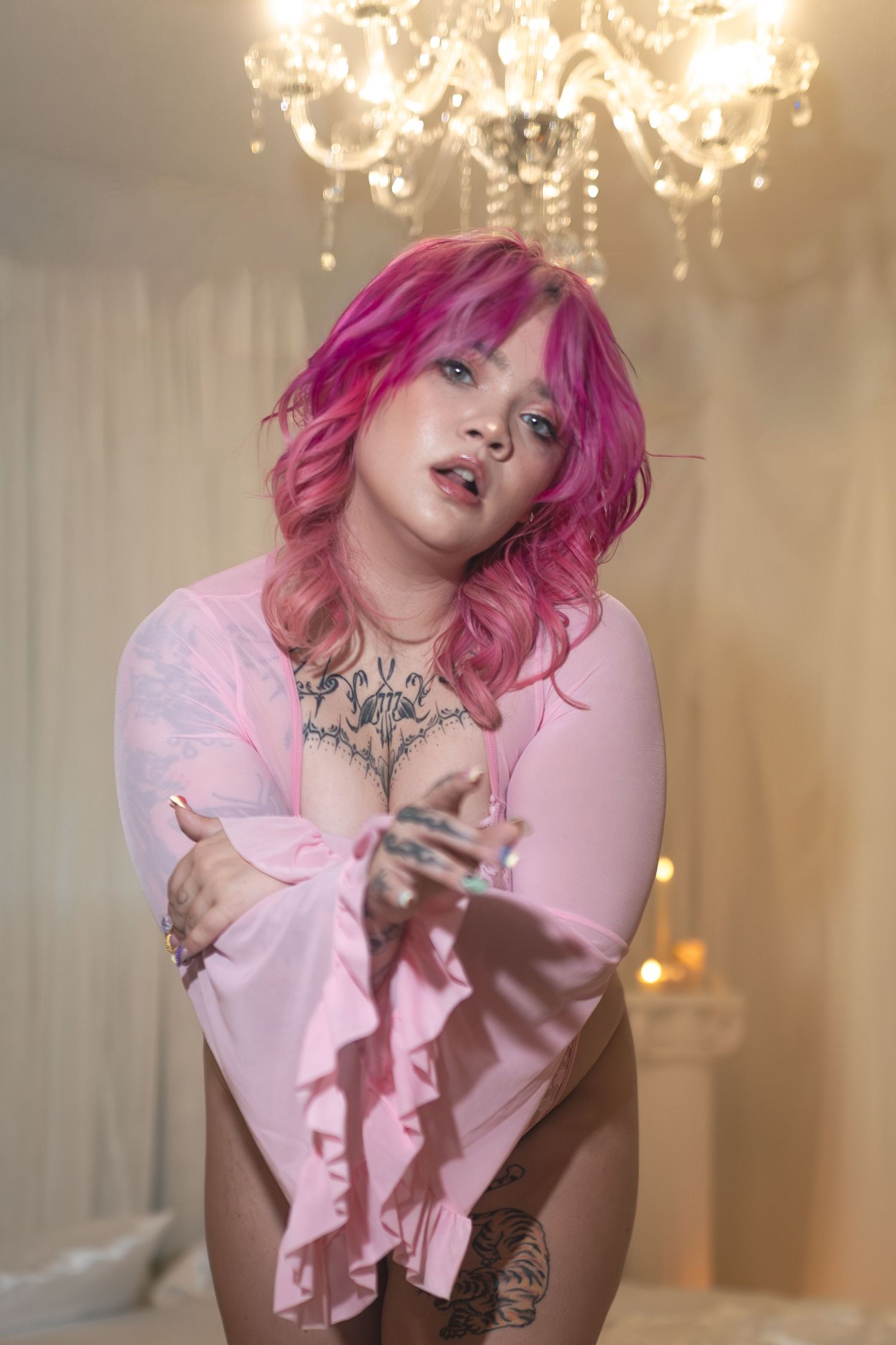 Tattoooed woman with pink hair in sheer pink lingerie romantic candlelit boudoir portrait.